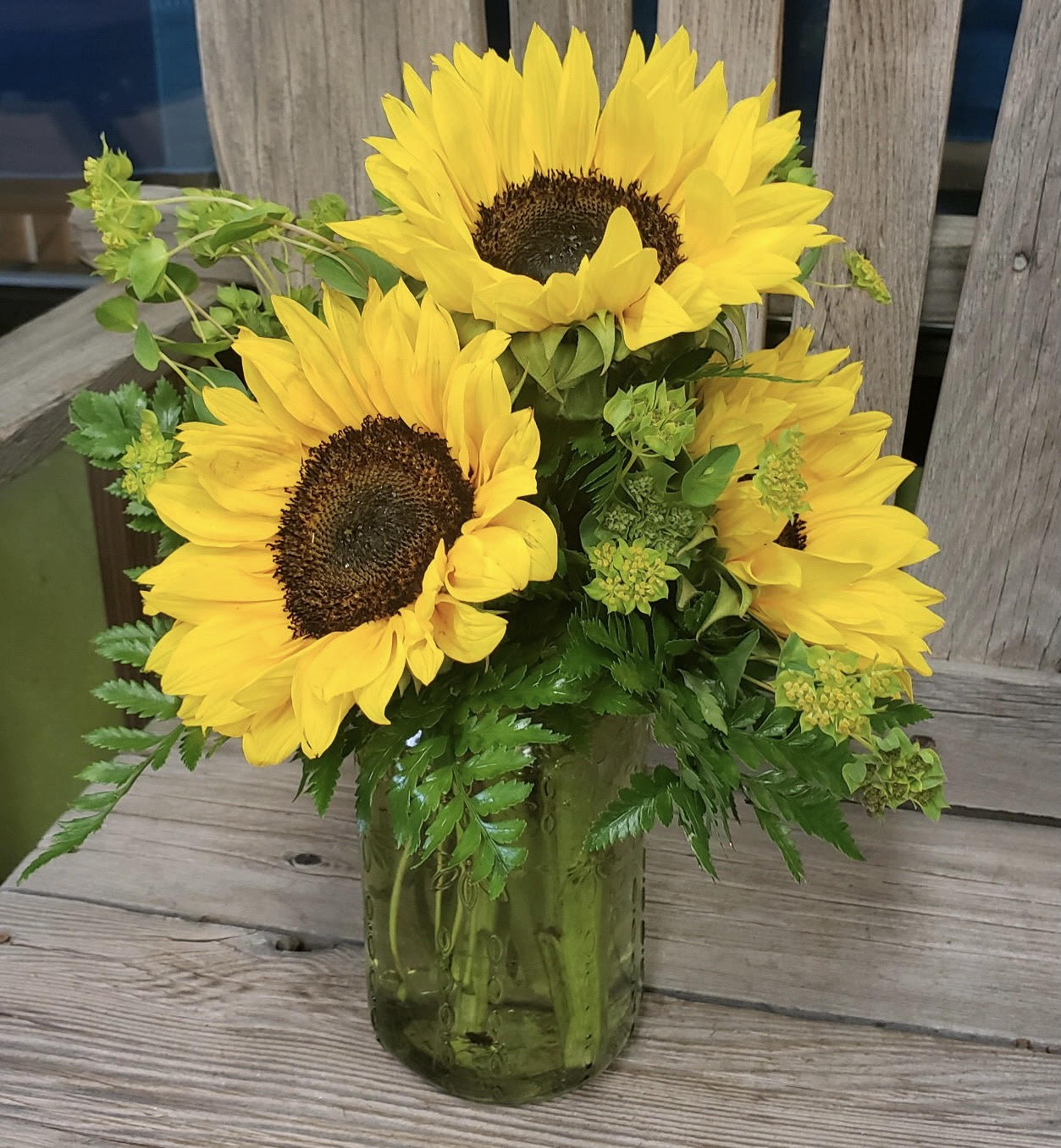Sunniest of the Sunnies - Who would say no to a jar full of pure sunshine?! Brighten someones day with just that.   This arrangement is pure and simple with flowing fresh greens and bright as sunshine sunflowers. Your arrangement arrives in a Mason type jar. 