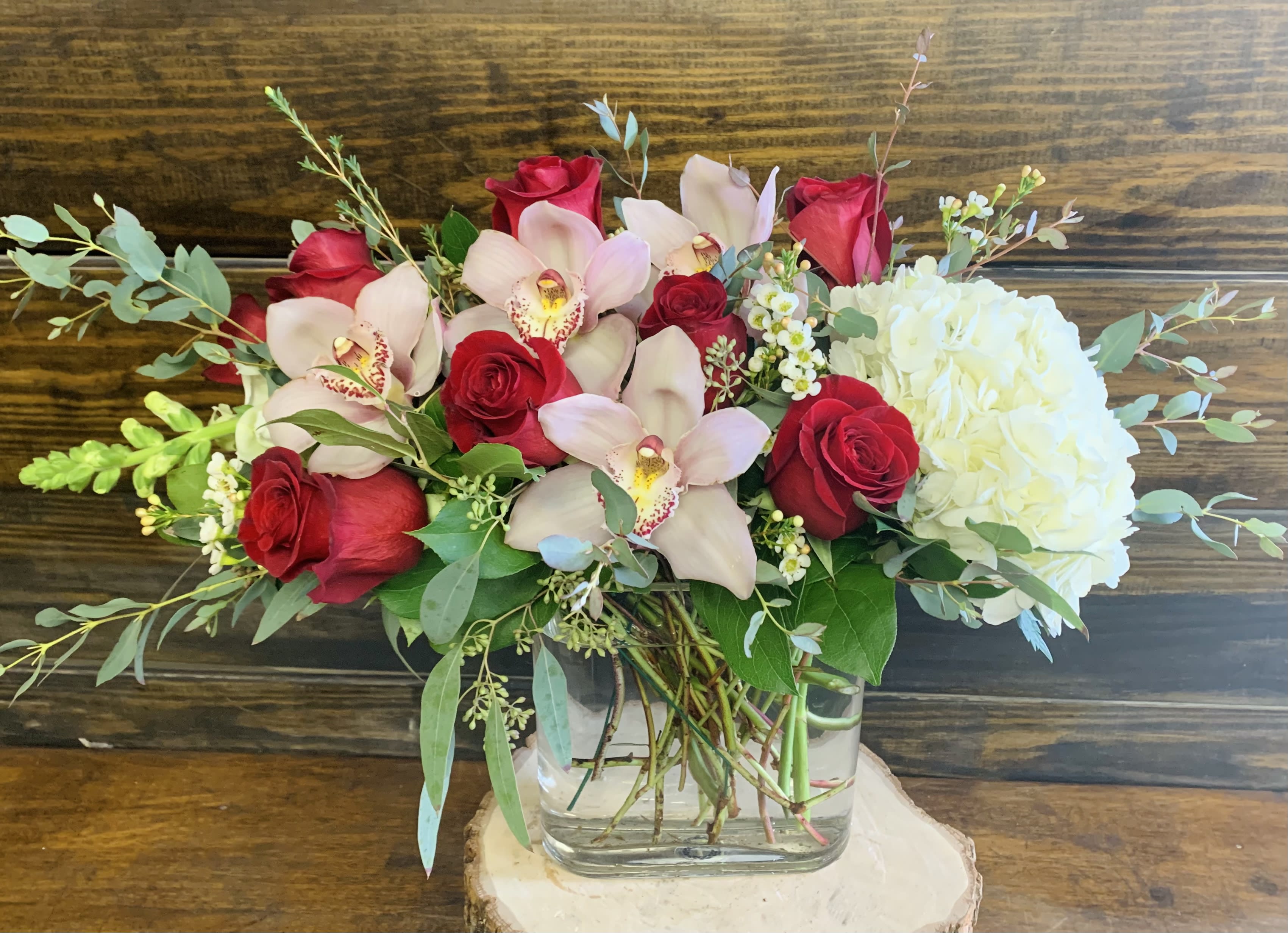 Bouquet of red roses, pale orchids, and white hydrangea in a glass vase