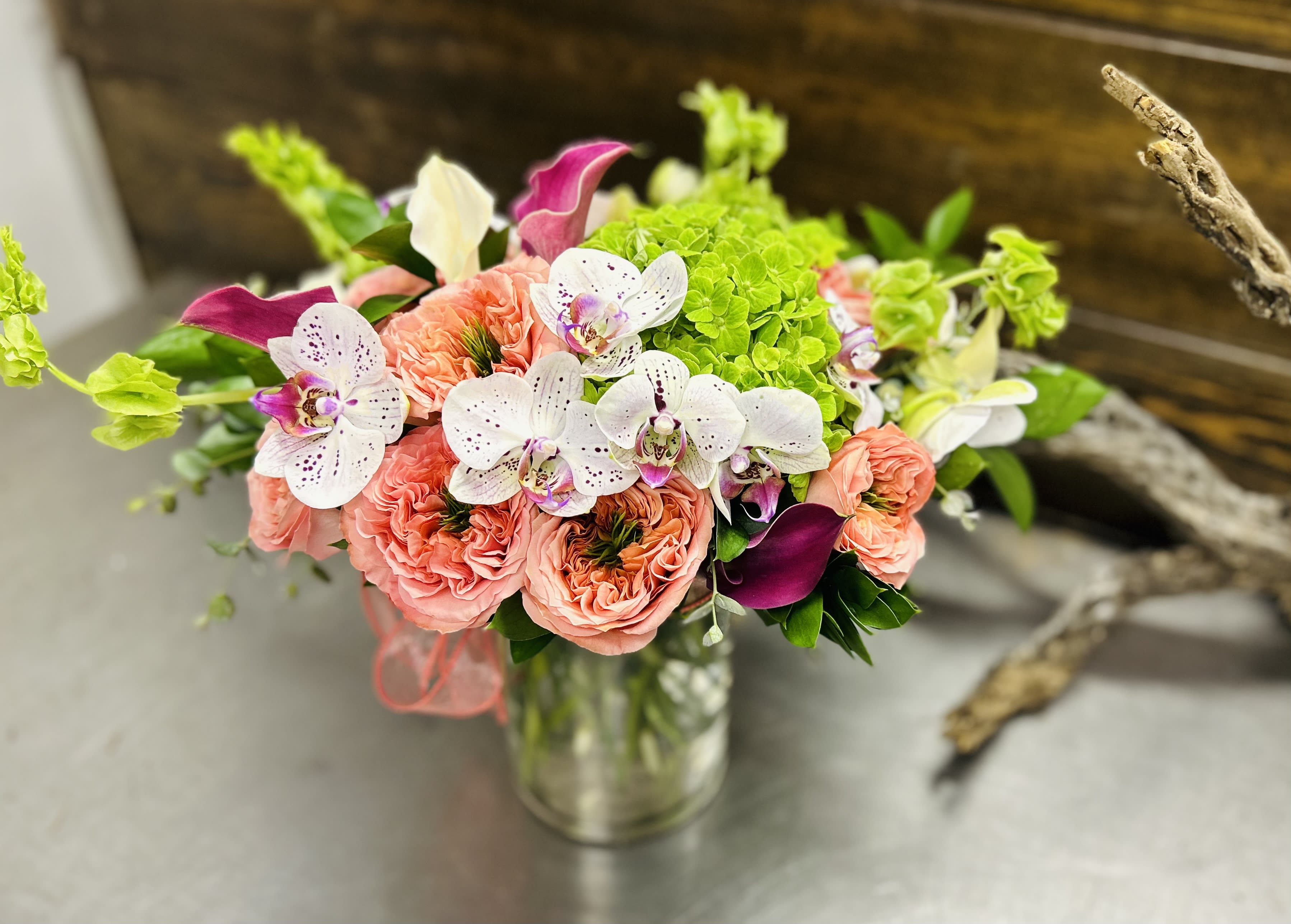 Bouquet of coral roses, white orchids, and green hydrangeas in a glass vase