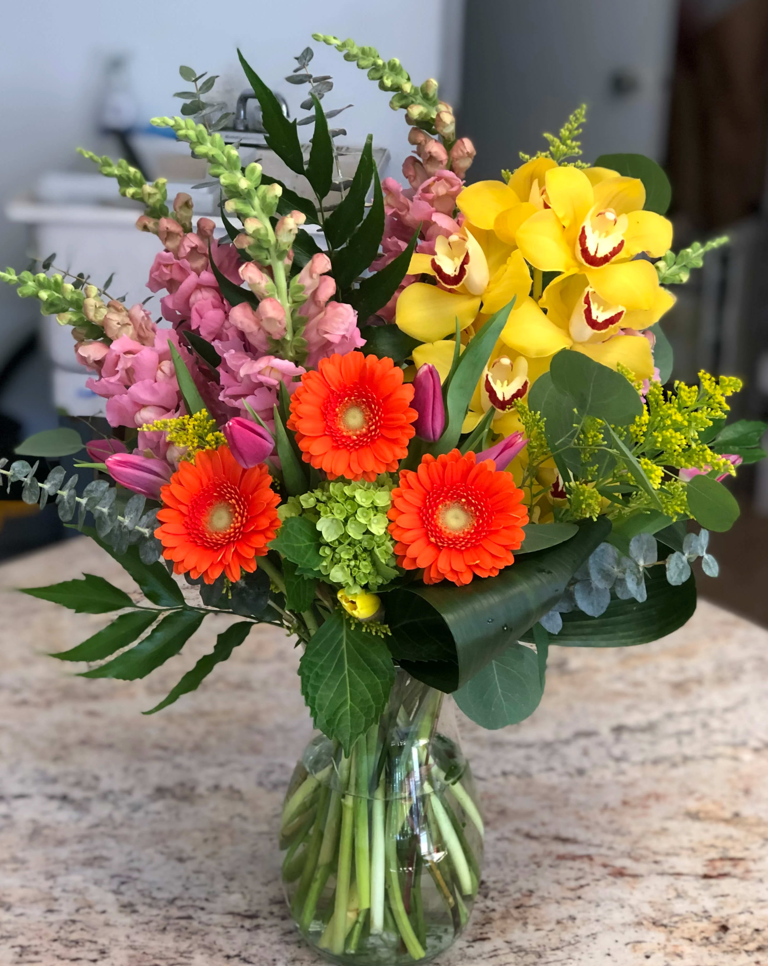 Mixed bouquet with yellow orchids, orange gerbera daisies, and pink snapdragons in a glass vase