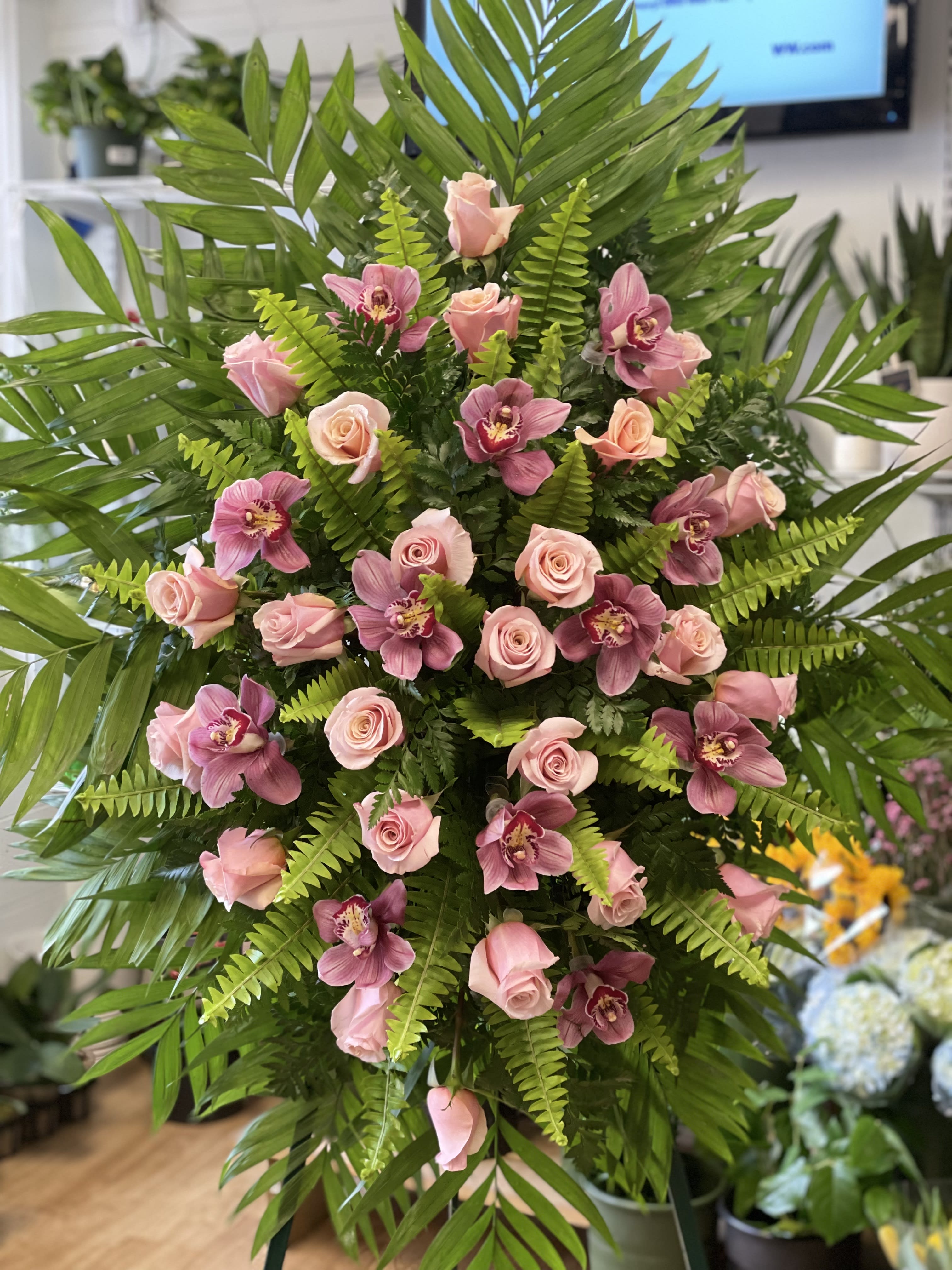 Pink roses and orchids arranged in a tall standing display with fern foliage.