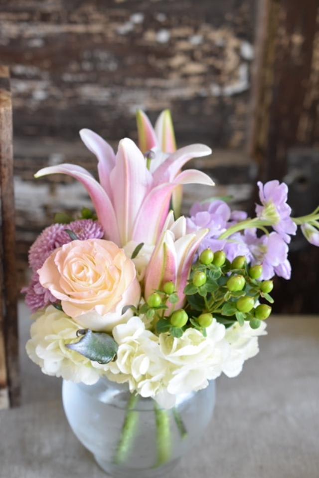 Pink lilies and roses arranged in a glass vase with white blooms