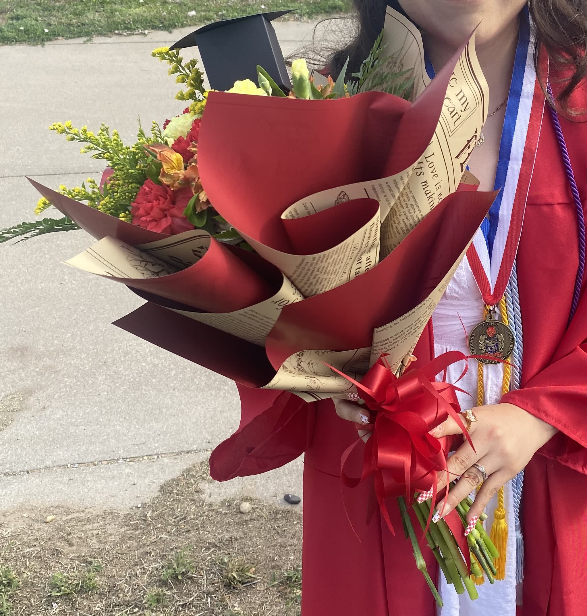 Graduate holding a wrapped bouquet of mixed flowers with a red ribbon