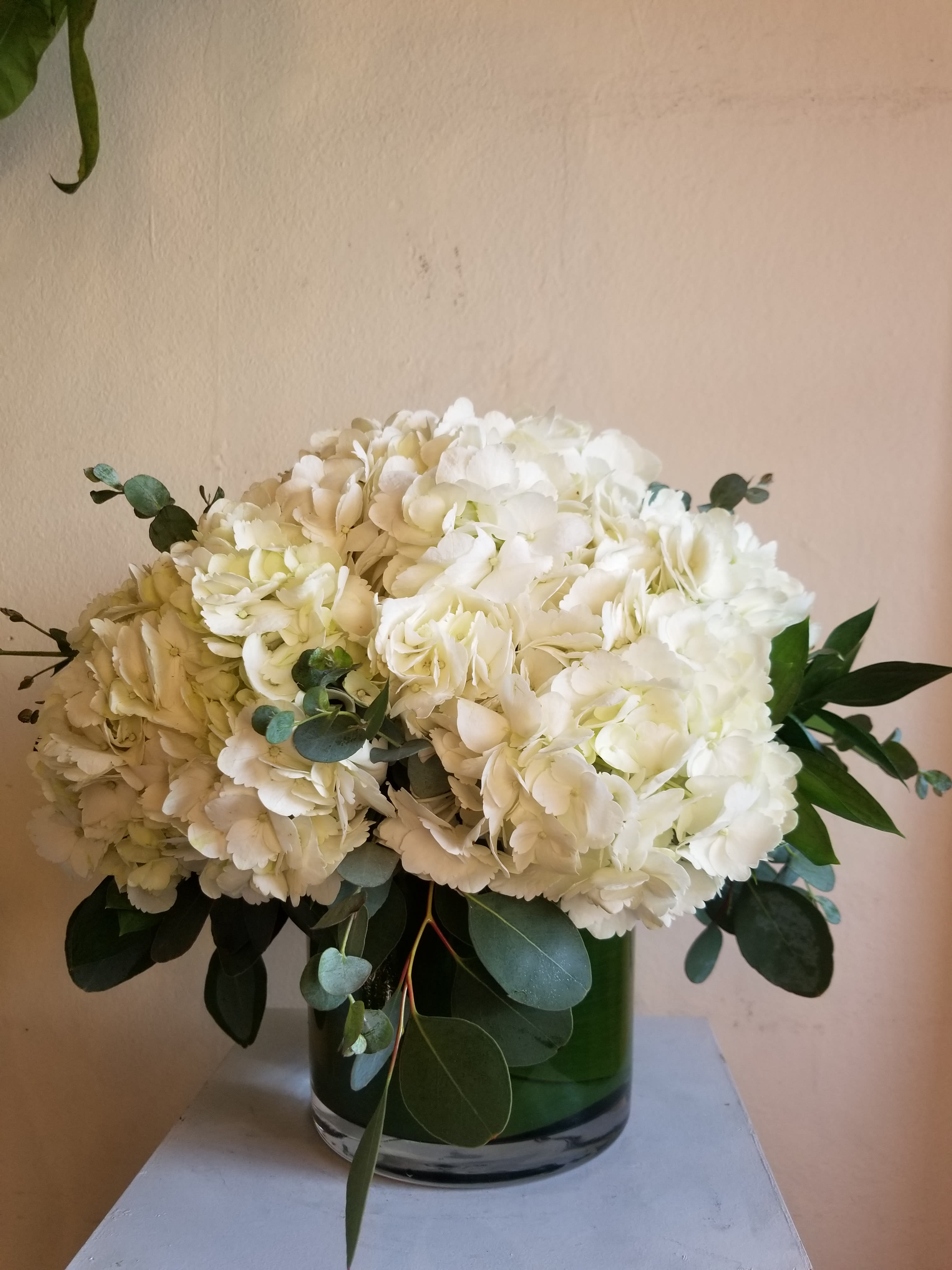 White hydrangea bouquet in a green glass vase with eucalyptus