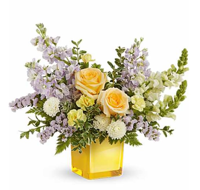 TF Sunshine Dreams - Teleflora's Sunshine Dreams Bouquet features yellow roses, yellow miniature carnations, lavender stock, white button spray chrysanthemums, white snapdragons, and lavender statice, accented with leatherleaf fern and oregonia. Arranged in a yellow glass cube vase.