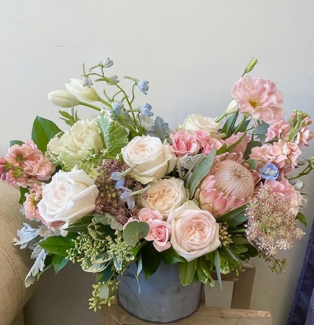 Pastel bouquet of roses, lisianthus, and protea in a gray vase