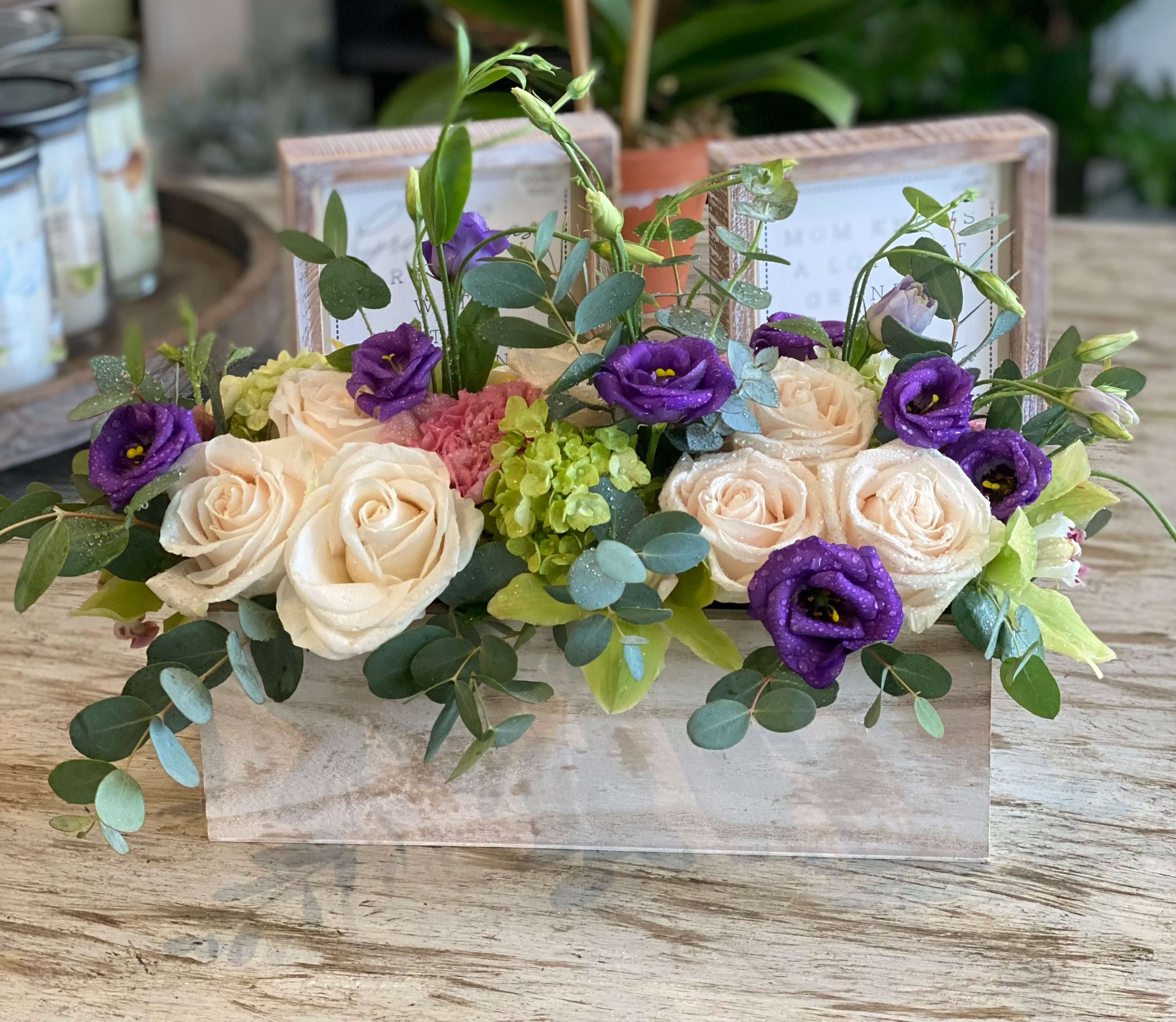 Cream roses and purple blooms arranged in a low wooden box