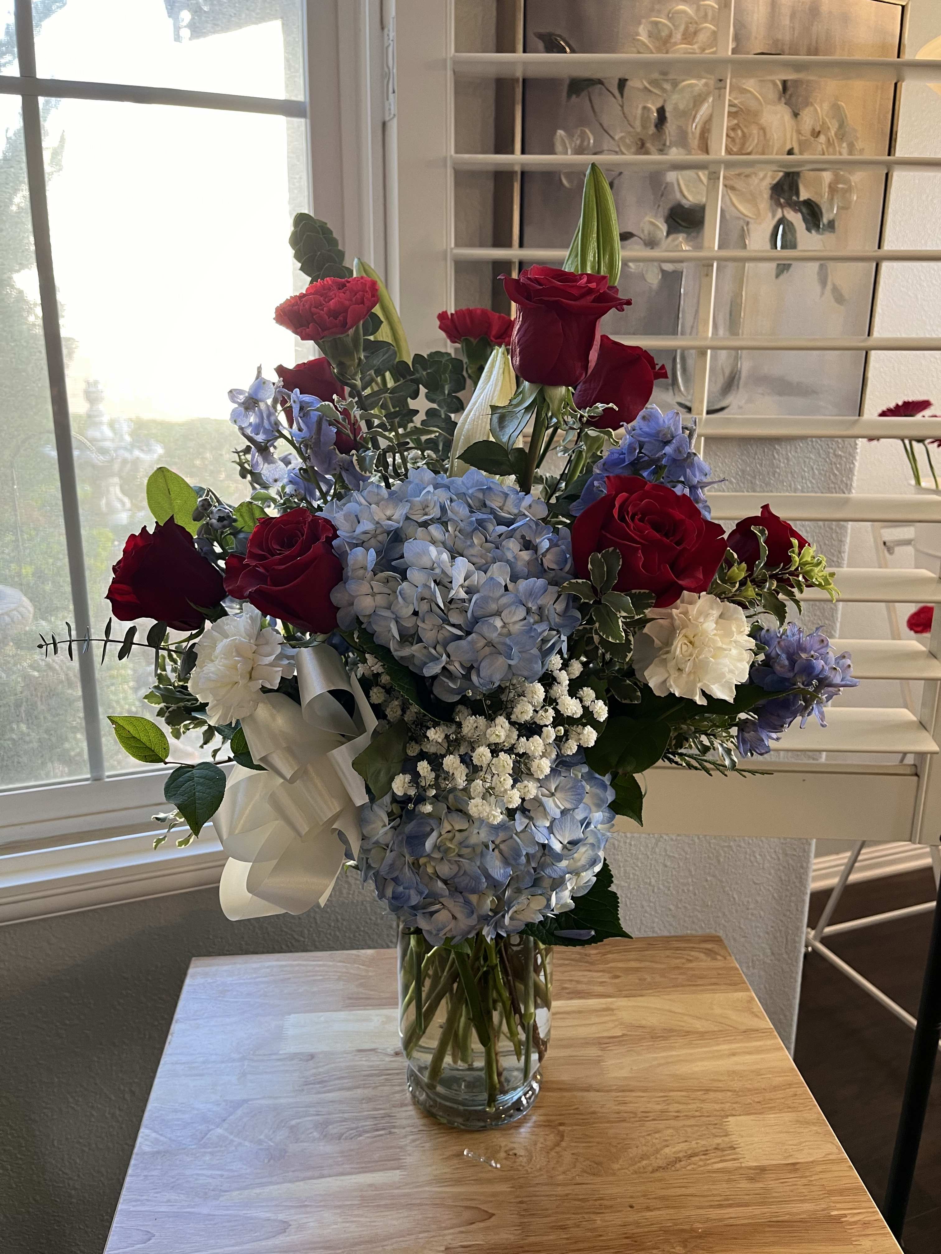 Mixed bouquet of red roses, blue hydrangeas, and white flowers in a glass vase
