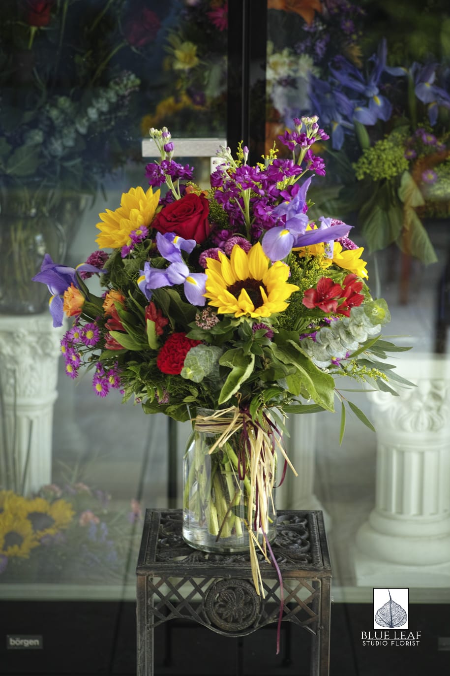 Mixed bouquet with sunflowers, roses, and purple iris in a glass vase