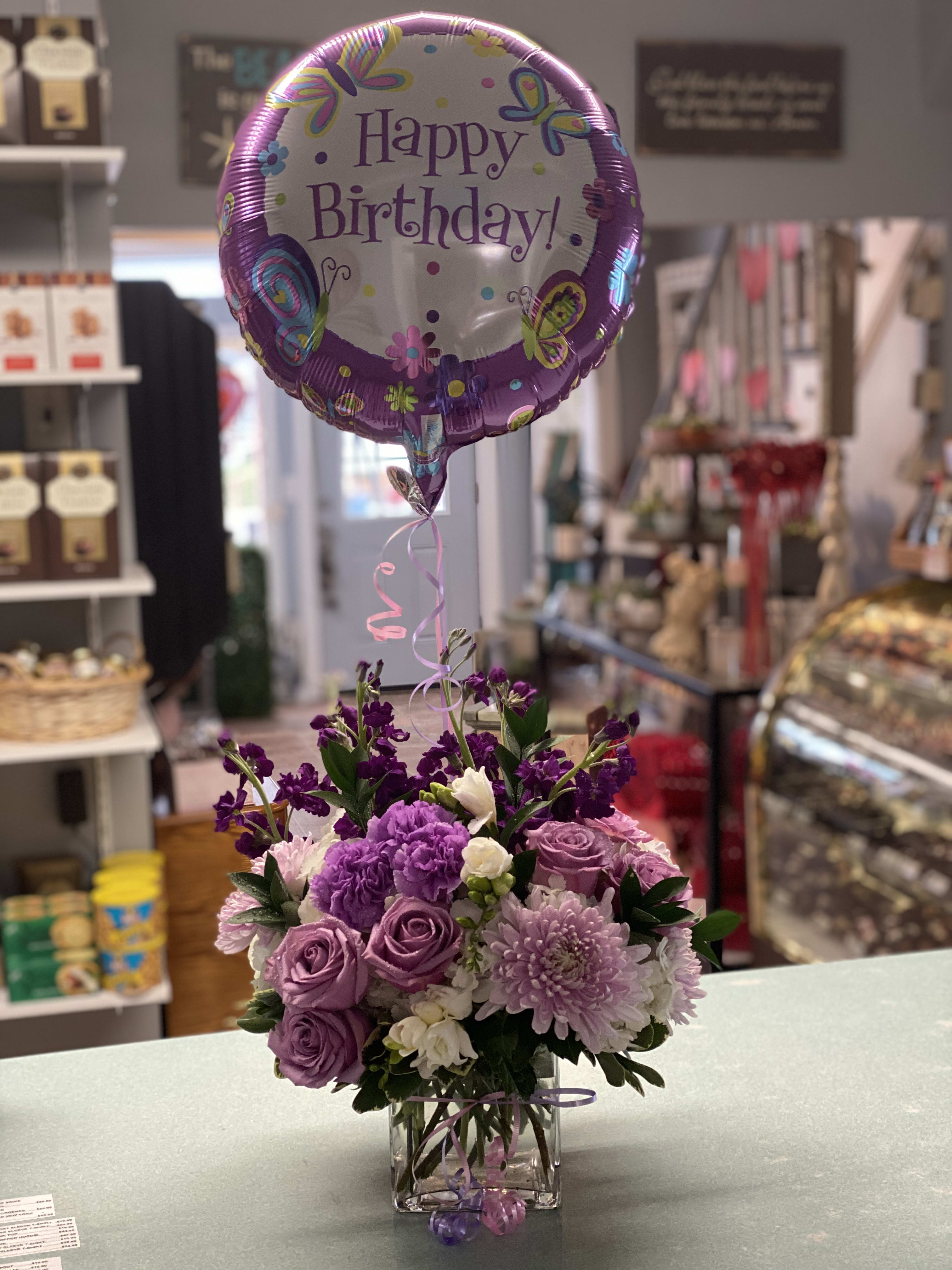 Purple flower arrangement with a Happy Birthday balloon in a glass vase