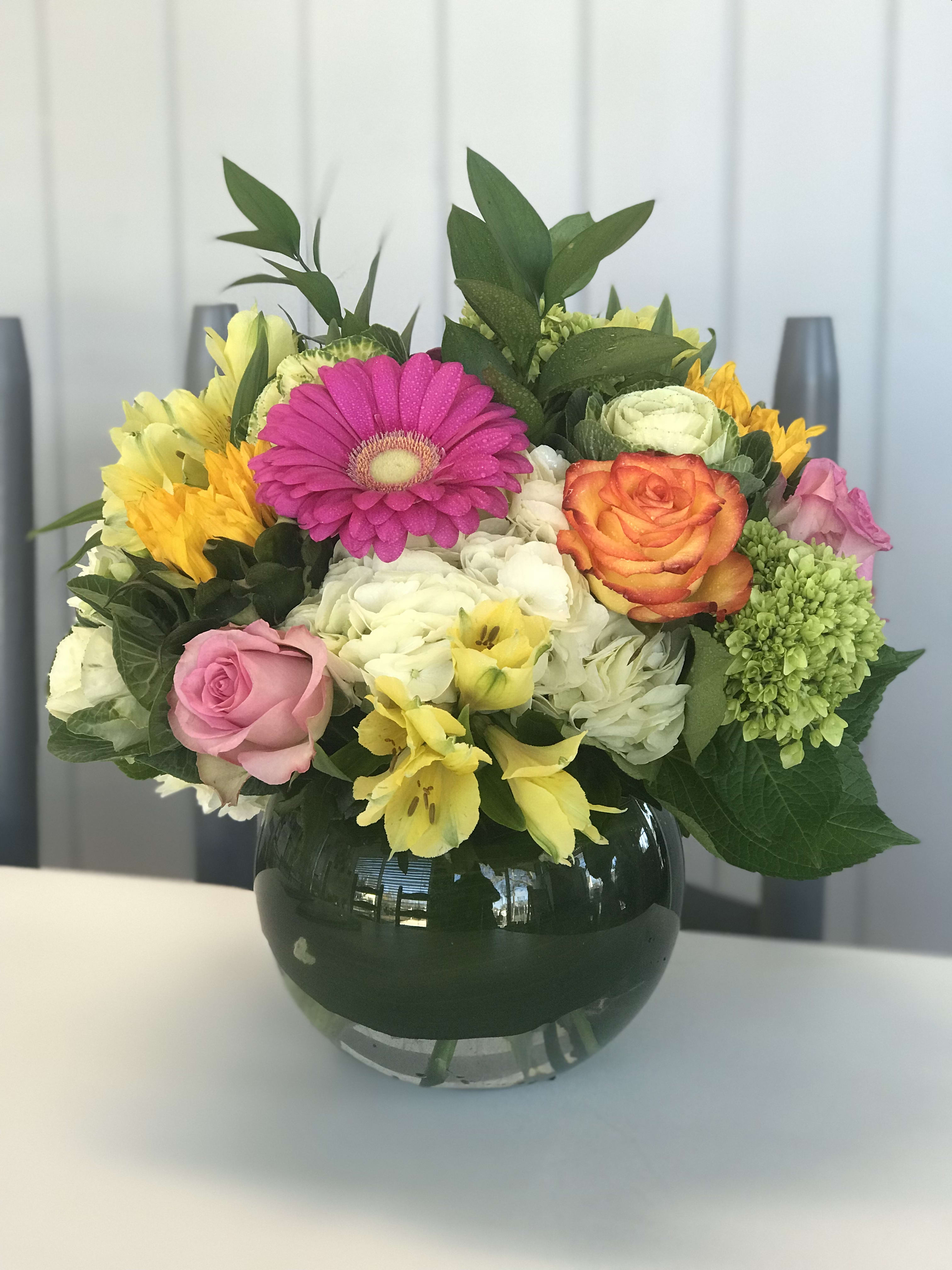 Roses, Gerberas and Everything Nice - Lush white premium Hydrangea are enhanced by hot pink Gerberas, pink and orange roses, and a burst of alstroemeria in a 6 inch bubble ball lined with aspidistra greens.