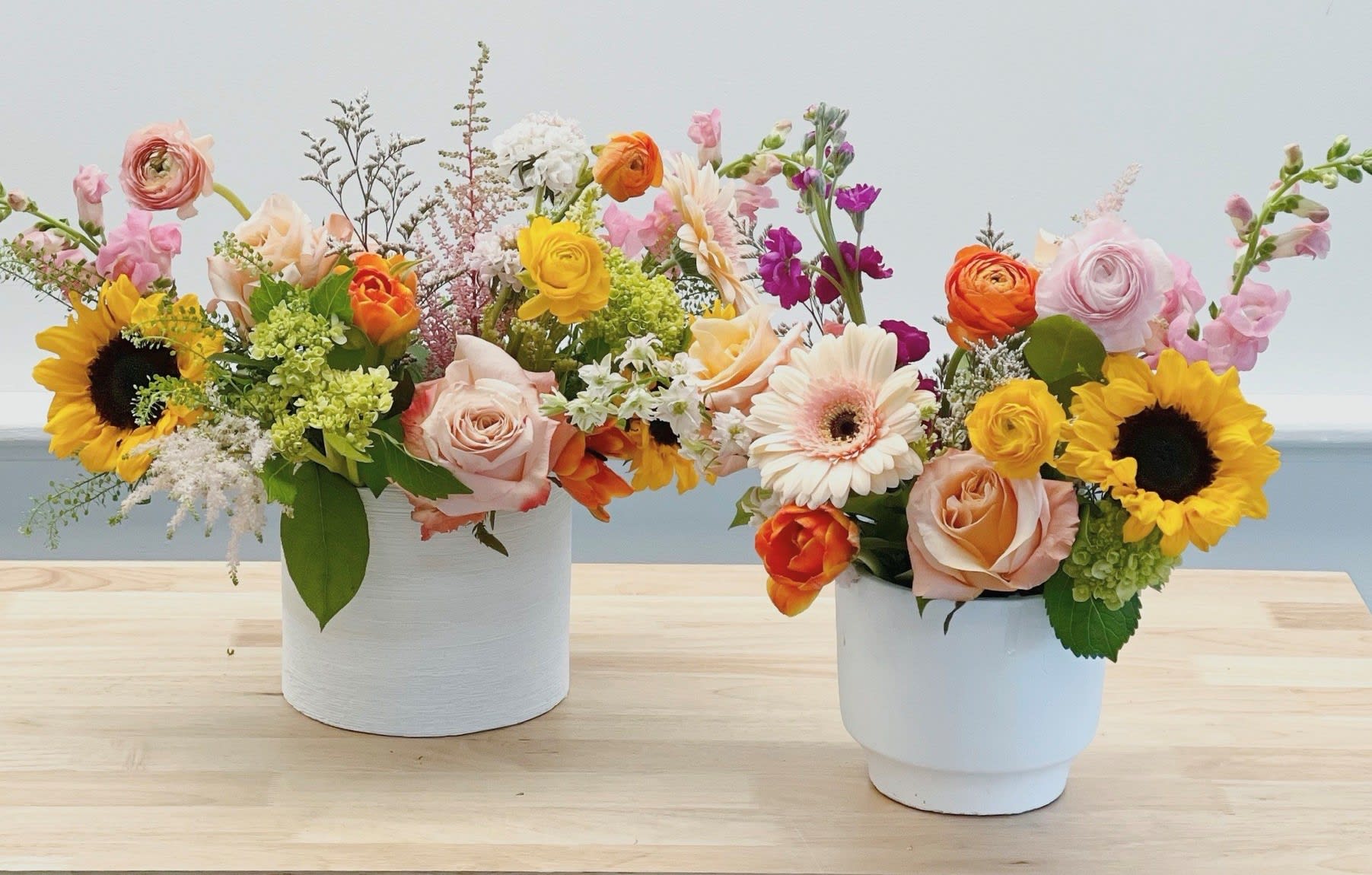 Two colorful flower arrangements in white pots on a table