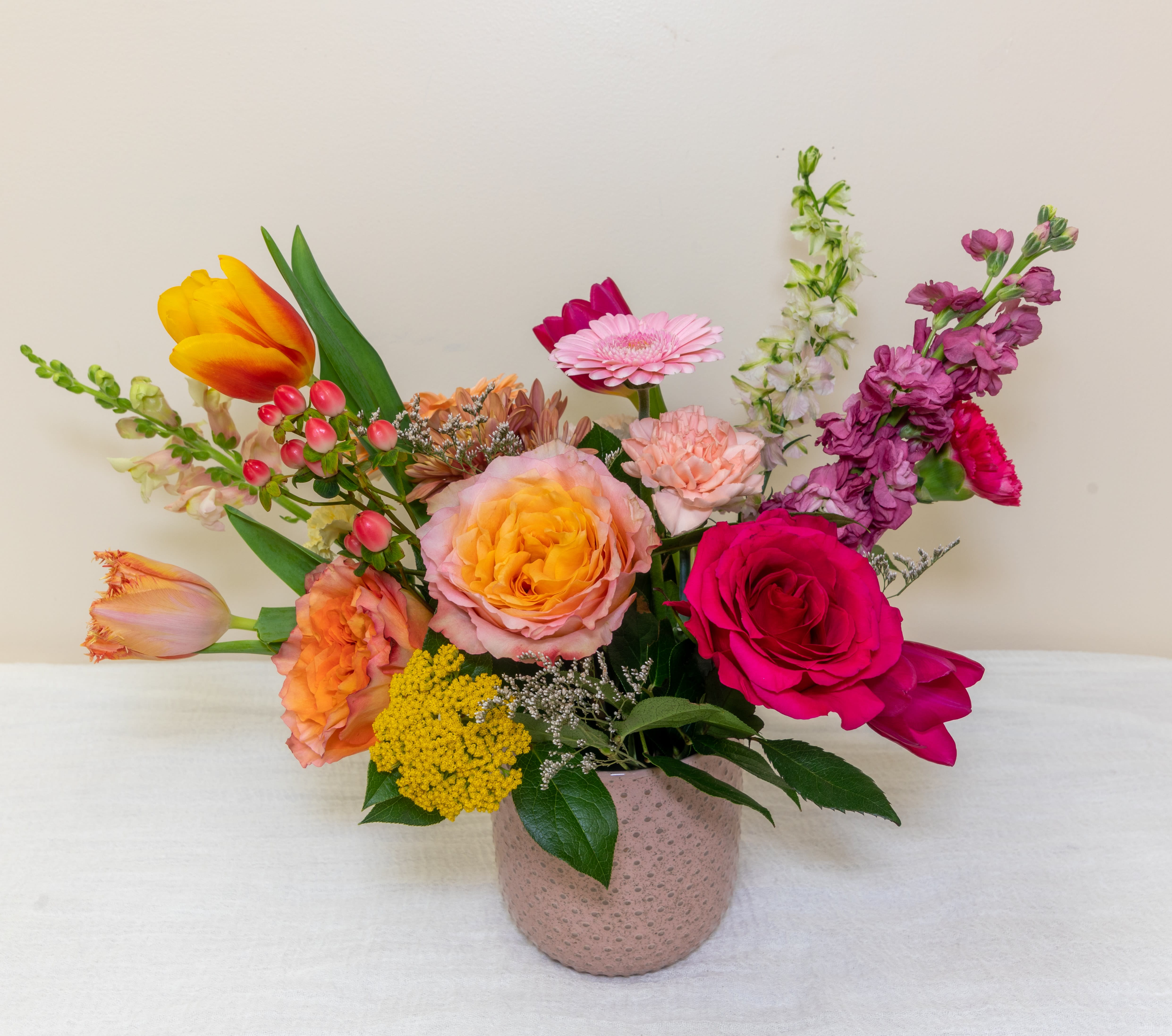 Mixed bouquet in a pink textured vase with roses, tulips, and gerbera daisies