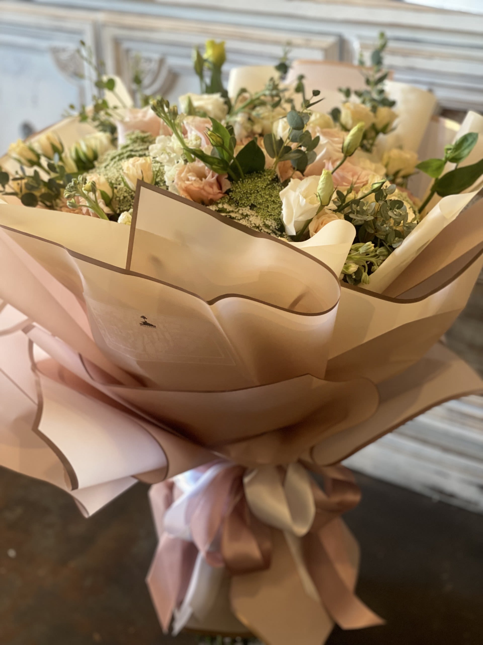 Champagne Whisper  - Soft ivory and blush blooms with fresh greenery, wrapped in elegant soft pink paper and finished with a flowing ribbon. Pure elegance in every petal.