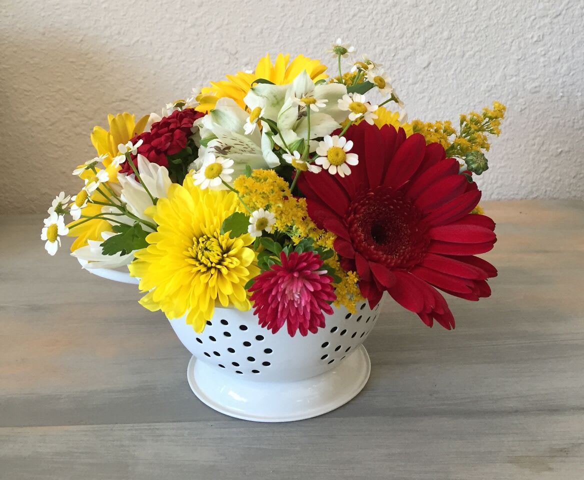 Mixed bouquet of daisies and chrysanthemums in a white colander-style vase