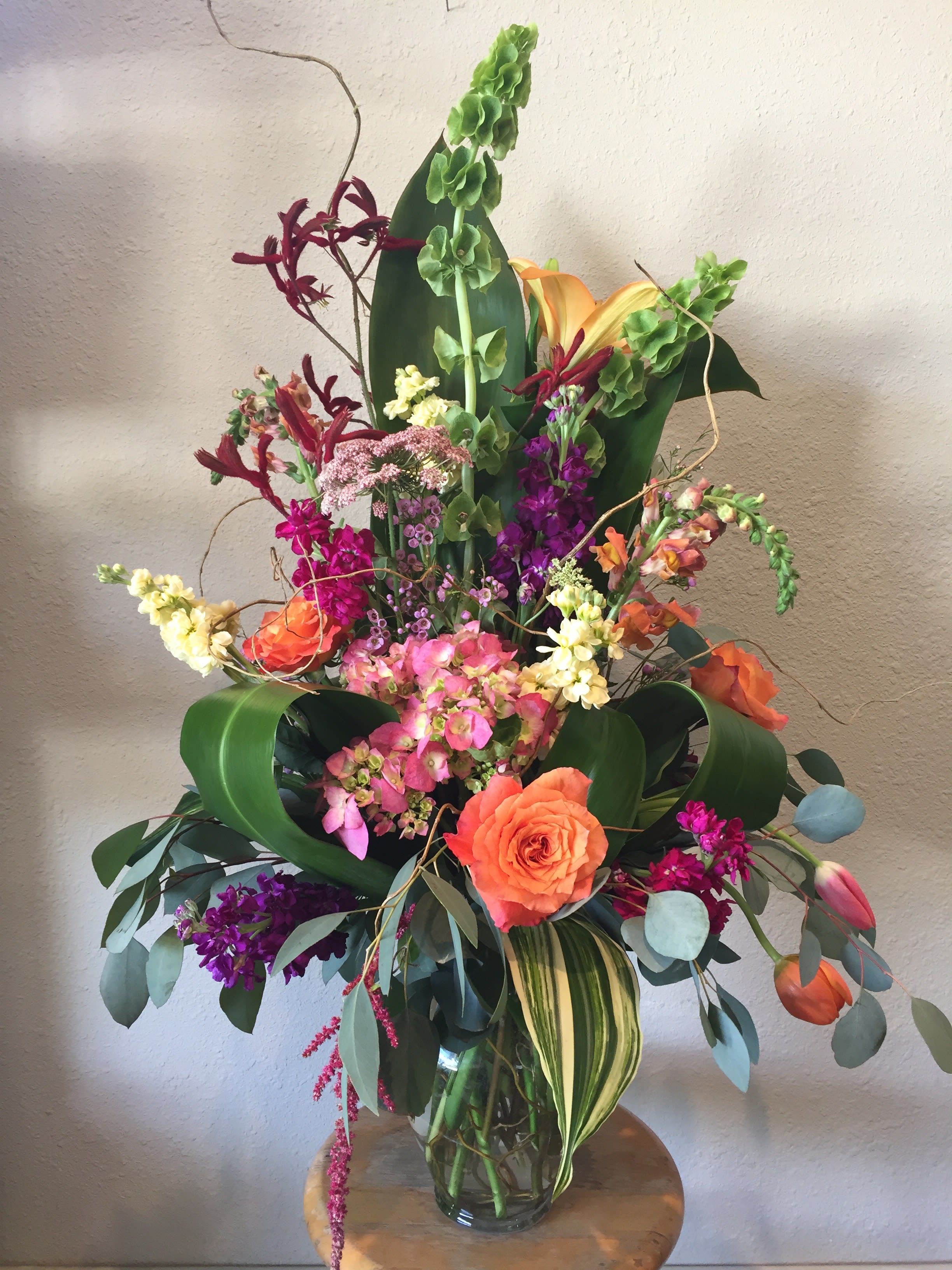 Tall mixed bouquet in a glass vase with orange, pink, purple, and green flowers