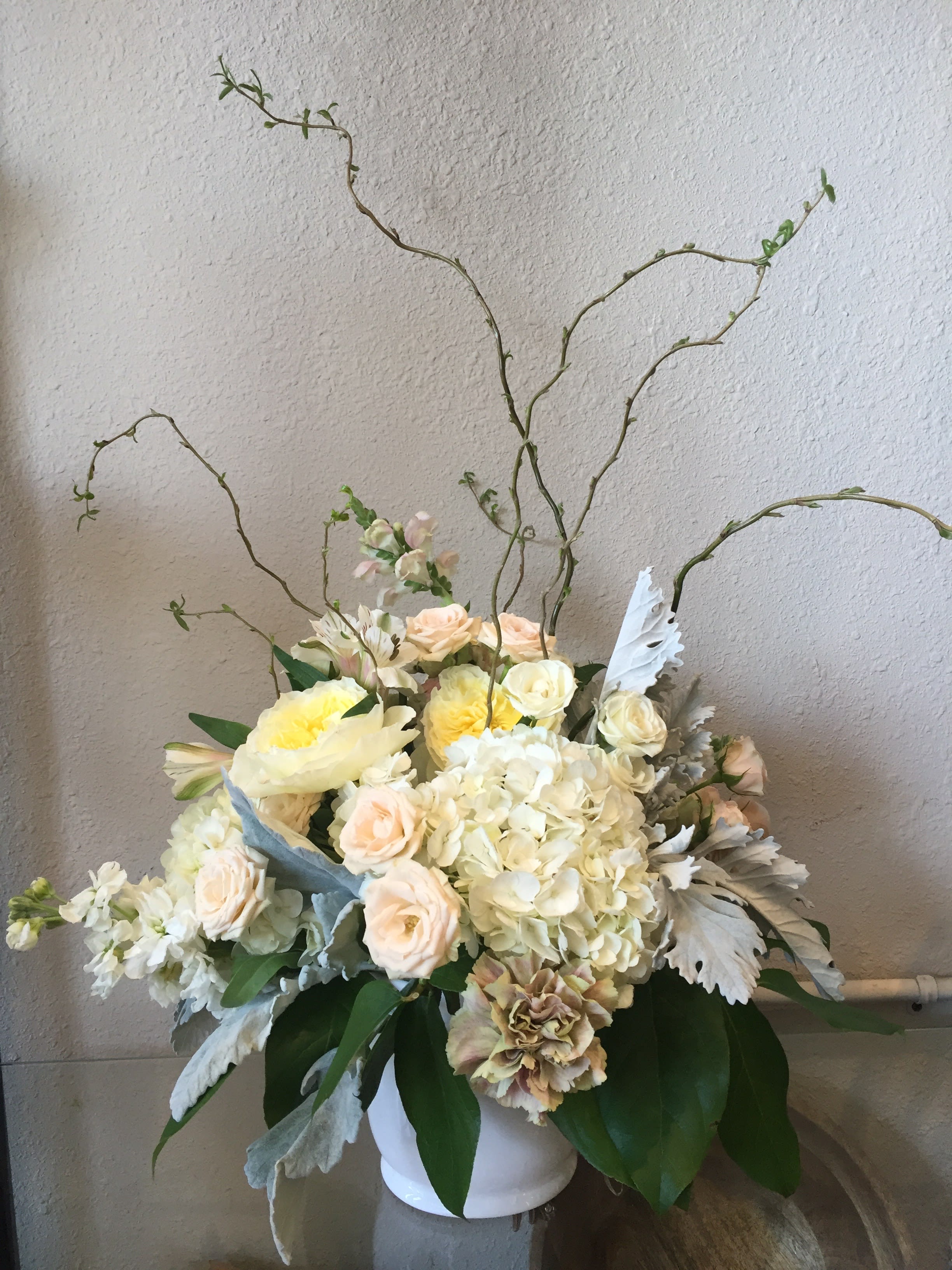Cream and blush floral arrangement in a white vase with tall curly branches