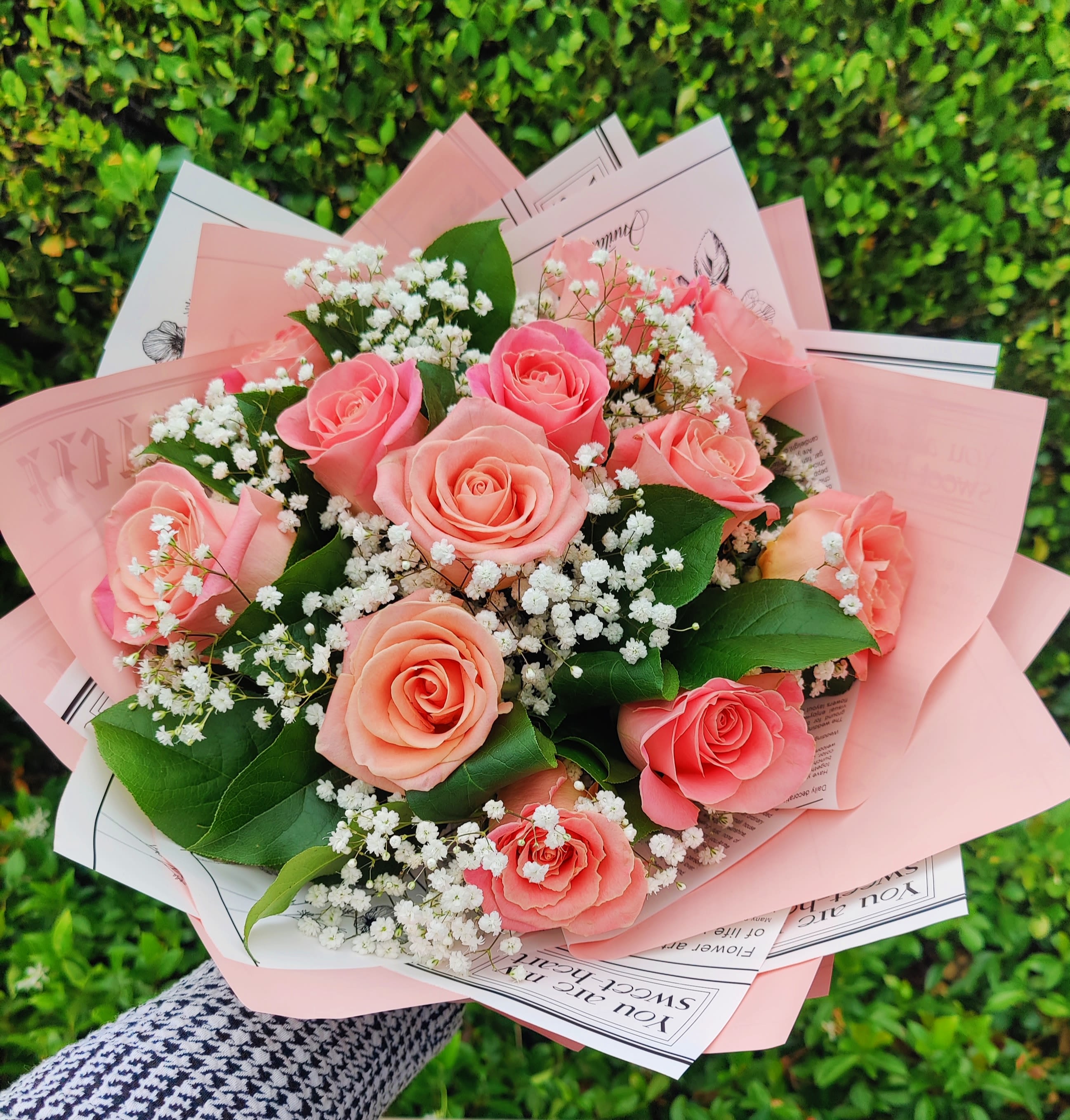 Hand-tied bouquet of peach roses and white filler flowers wrapped in pink paper