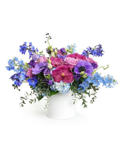Low arrangement of pink roses and purple and blue blooms in a white cylinder vase