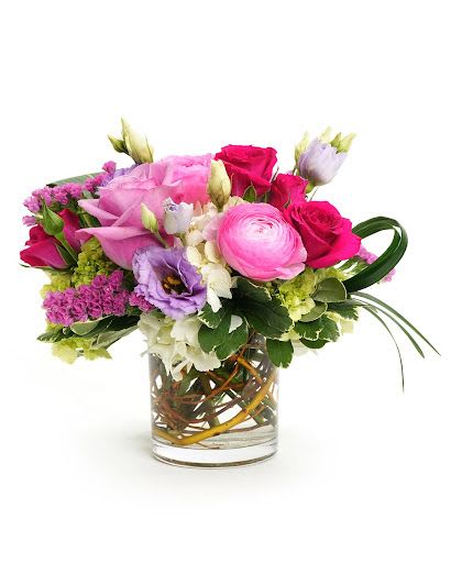 Low glass vase of pink roses, ranunculus, and mixed purple and white flowers in a compact arrangement