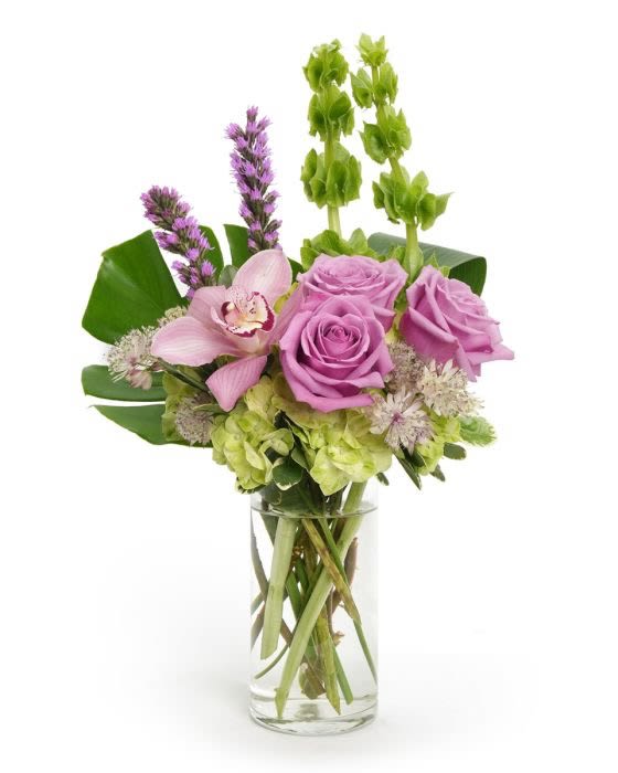 Tall arrangement of lavender roses, green hydrangea, Bells of Ireland and a pink orchid in a clear glass vase