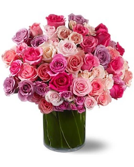 Arrangement of pink, white, and lavender roses in a clear cylinder vase wrapped with green leaves
