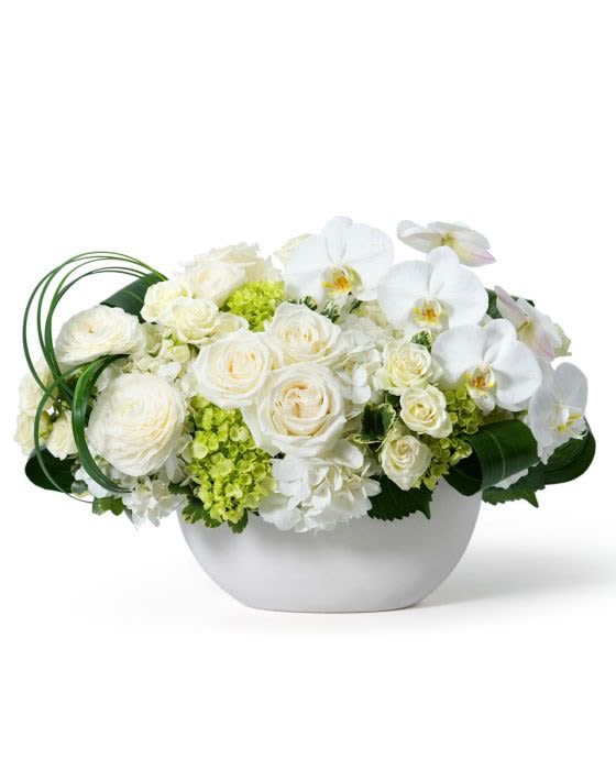Low white bowl of white roses, hydrangeas, and orchids with light green accents.