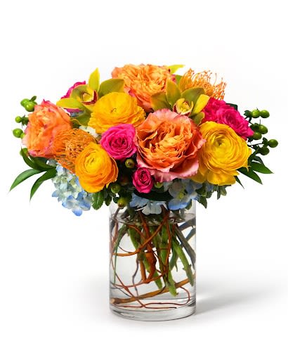 Bright orange, yellow, and pink flower arrangement in a clear glass cylinder vase with submerged branches.