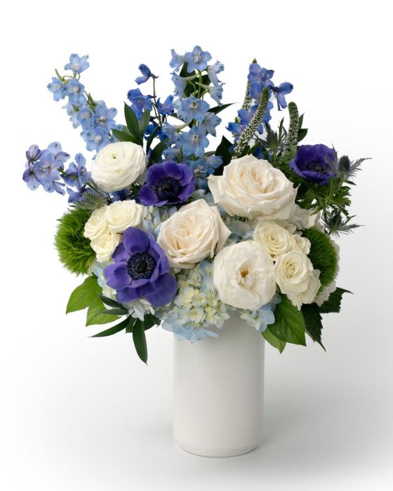 White and blue flower arrangement with roses and anemones in a tall white cylinder vase
