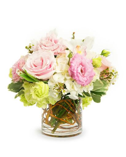 Low arrangement of pink roses and mixed pastel flowers in a clear glass vase with curly branches.