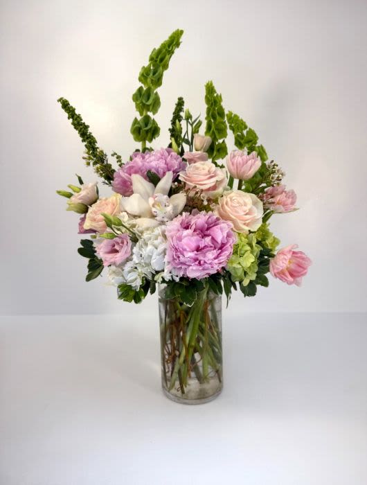 Tall pastel arrangement of pink peonies and roses with green Bells of Ireland in a clear glass vase