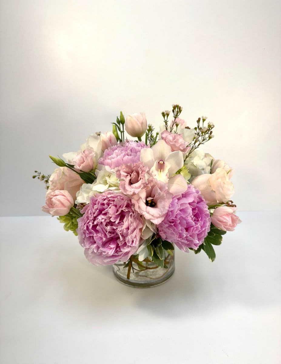 Low pink and white arrangement with peonies, tulips, and lisianthus in a clear glass vase