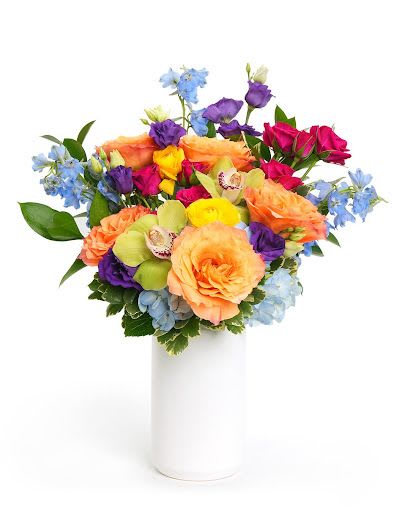 Colorful bouquet of peach roses and mixed bright blooms in a white cylinder vase