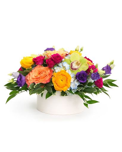 Low arrangement of bright mixed flowers in a white round vase
