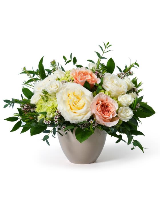 Low arrangement of white and peach roses with pale blooms in a round ceramic vase