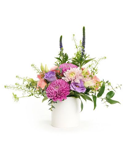 Mixed arrangement of pink and purple flowers with peach accents in a white cylinder vase