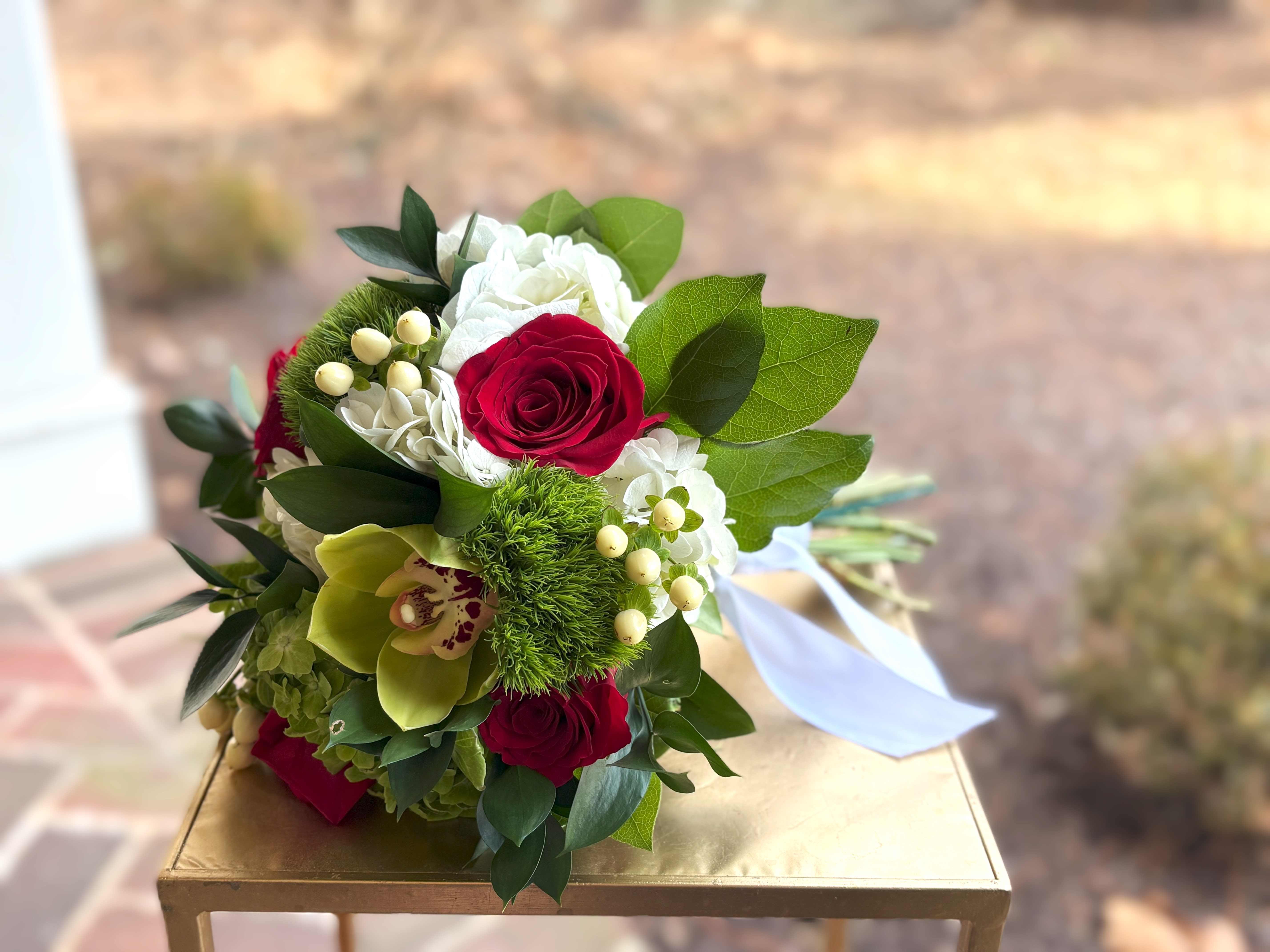 Hand-tied bouquet with red roses, white hydrangeas, green cymbidium orchid, and green dianthus tied with white ribbon