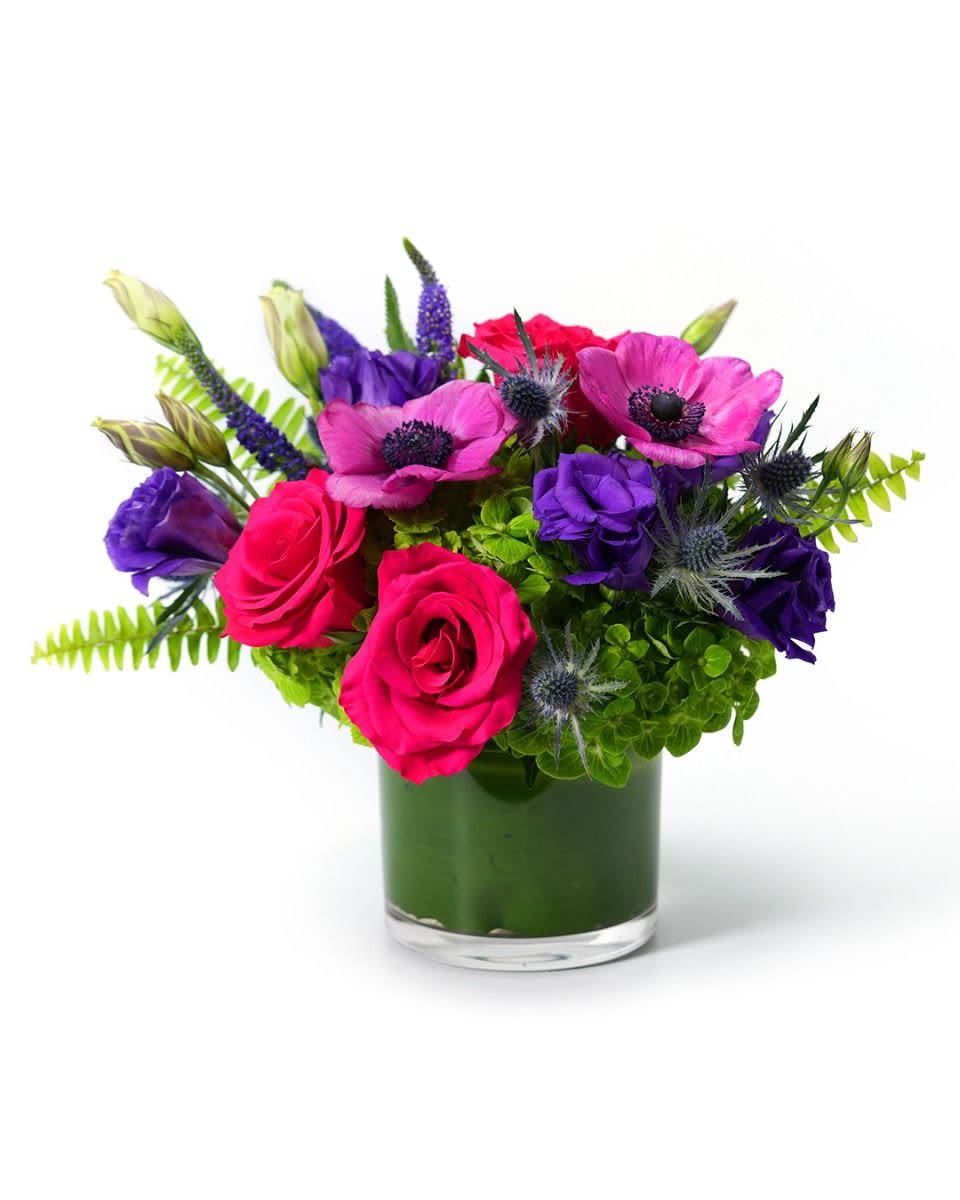 Low glass vase with hot pink roses, magenta anemones, purple flowers, and bright green blooms.