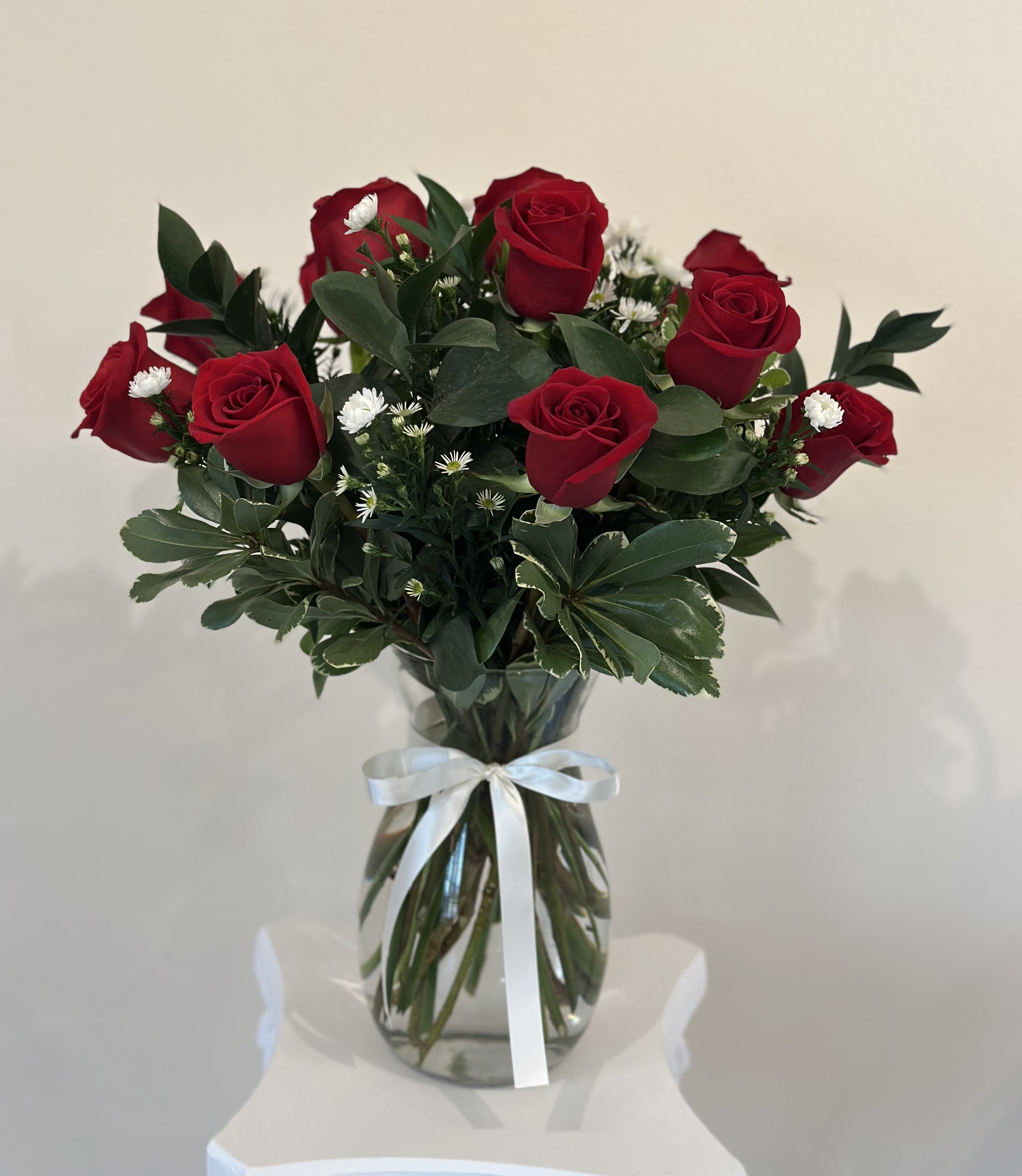 Bouquet of red roses and small white filler flowers in a glass vase with a white ribbon.