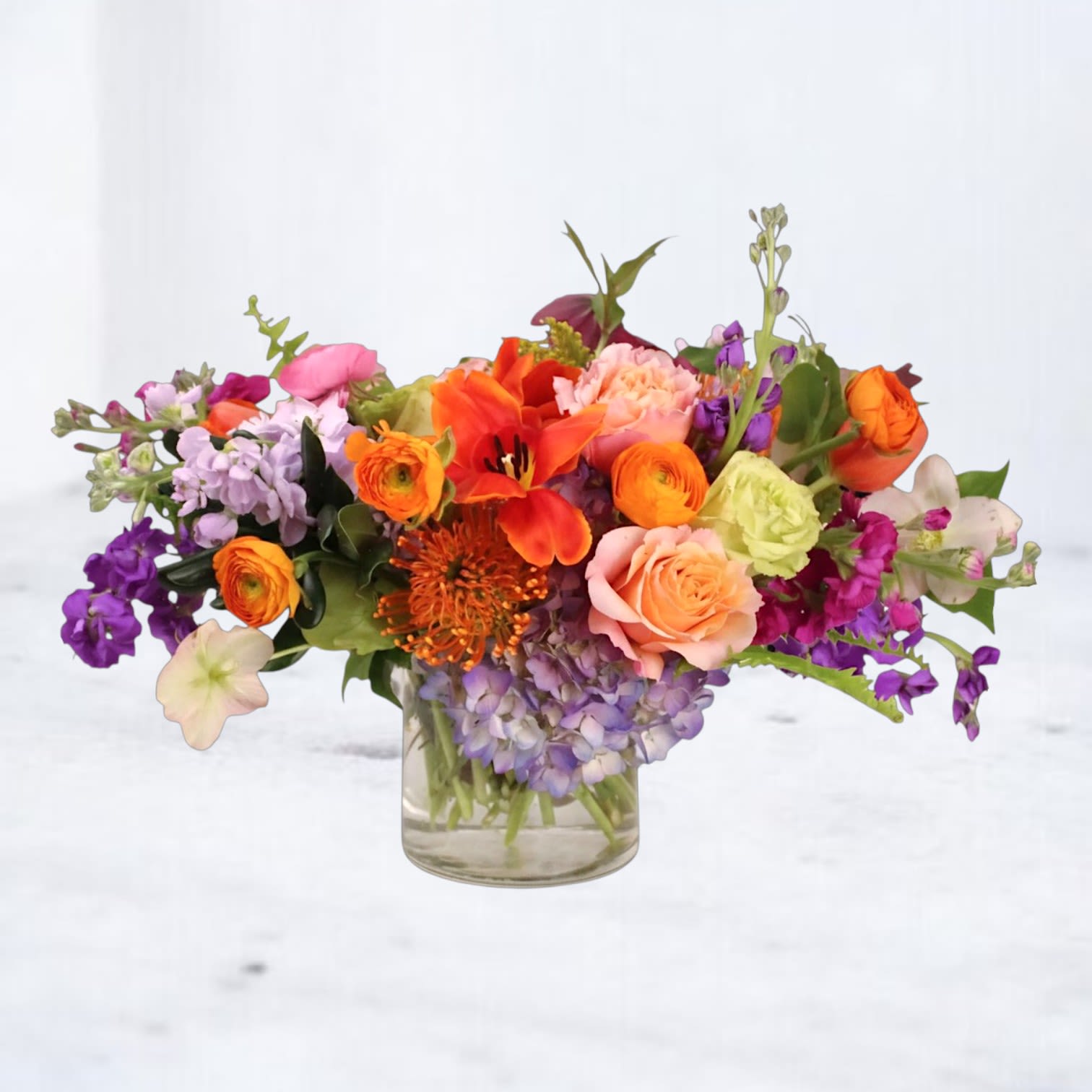 Social Hour - Social Hour is a vibrant, garden-inspired floral arrangement designed with bold color, airy movement, and a playful modern feel. Featuring a lively mix of peach roses, orange ranunculus, hot pink blooms, lavender stock, blue hydrangea, coral lilies, textural pincushion protea, and seasonal premium flowers, this design creates a layered, high-energy statement from every angle.  Designed in a clear glass vase with an intentionally organic silhouette, Social Hour blends bright citrus tones, soft pastels, and rich pops of purple for a fresh, contemporary look that feels both artistic and effortlessly celebratory.  Perfect for birthdays, thank-you flowers, celebrations, dinner parties, hostess gifts, or just because flower delivery, this arrangement brings instant color and personality into any space.  We proudly offer same-day flower delivery in Magnolia, The Woodlands, Montgomery, Conroe, Spring, Tomball, Houston, Willis, Plantersville, and surrounding Texas communities, with every arrangement handcrafted using premium seasonal blooms.  Due to seasonal availability, some flowers may be substituted with similar varieties of equal or greater value while preserving the overall style, palette, and design integrity.