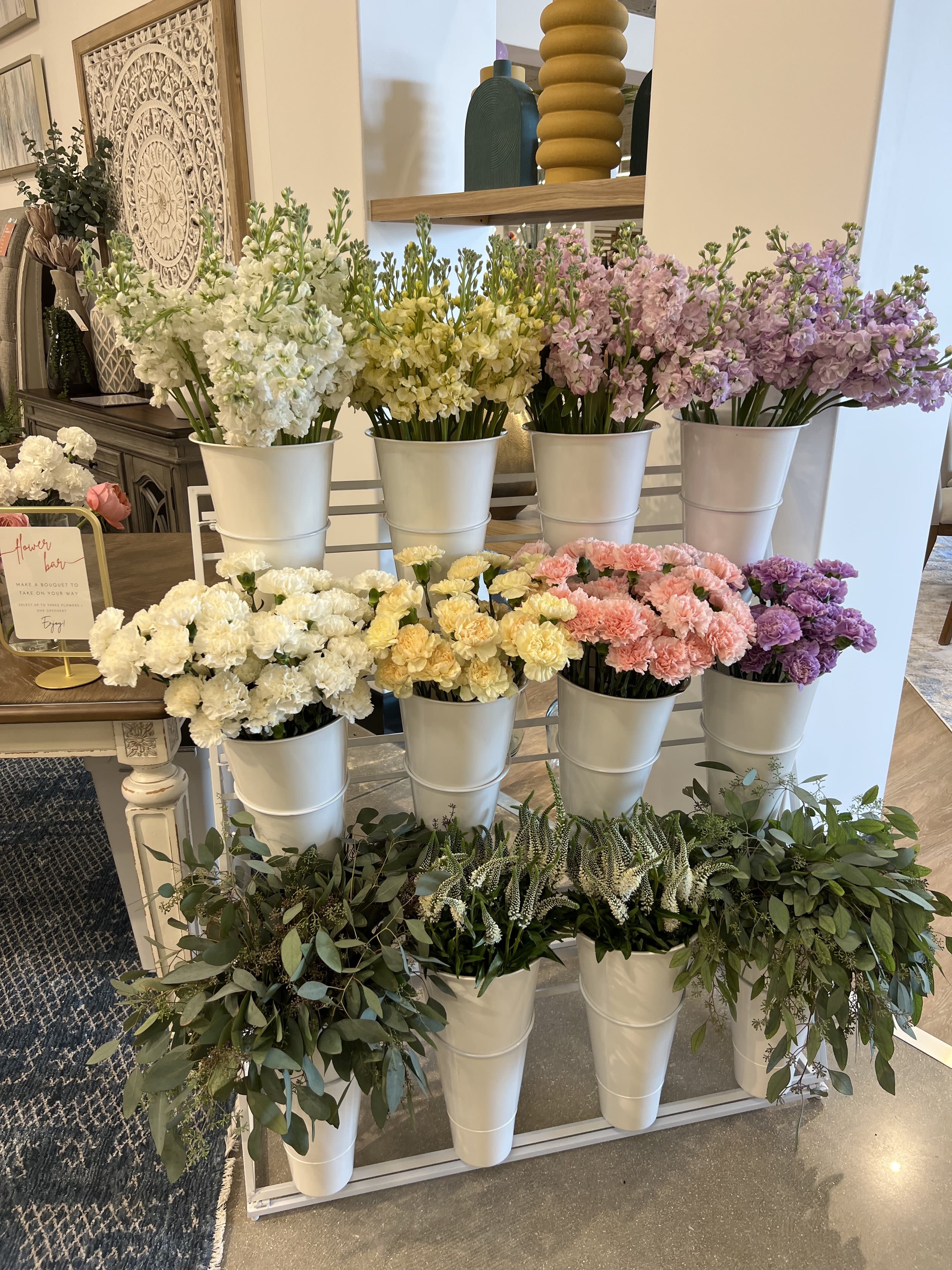 Rows of pastel flowers in white buckets on a display stand