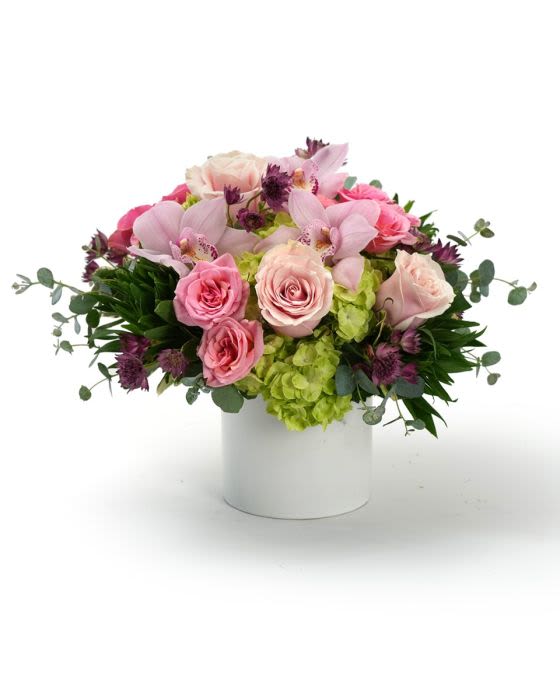Low arrangement of pink roses, orchids, and green hydrangeas in a white cylinder vase