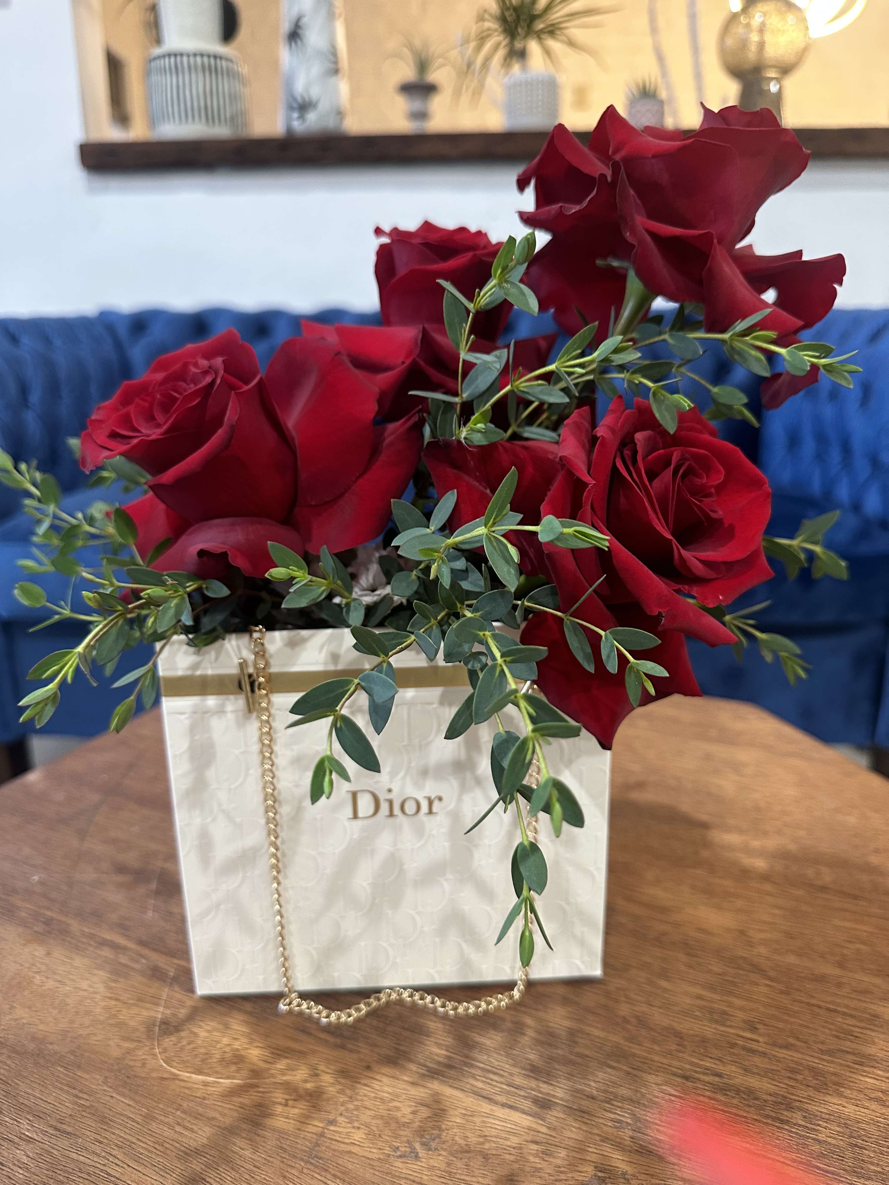 Red roses arranged in a white Dior gift bag with greenery.