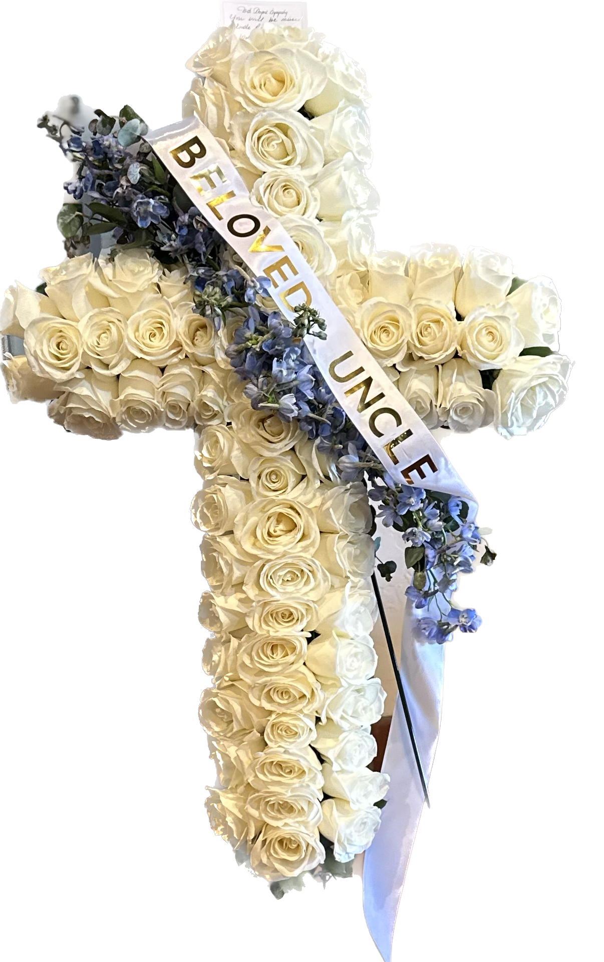 Holy Cross Standing Floral Spray  - Sending your loved ones comfort with this beauty filled with all white roses intricately placed throughout. Greenery and light florals intertwined across representing a sash draped over the Holy Cross  Note: Available in 3 colors Lavender, Pink and White