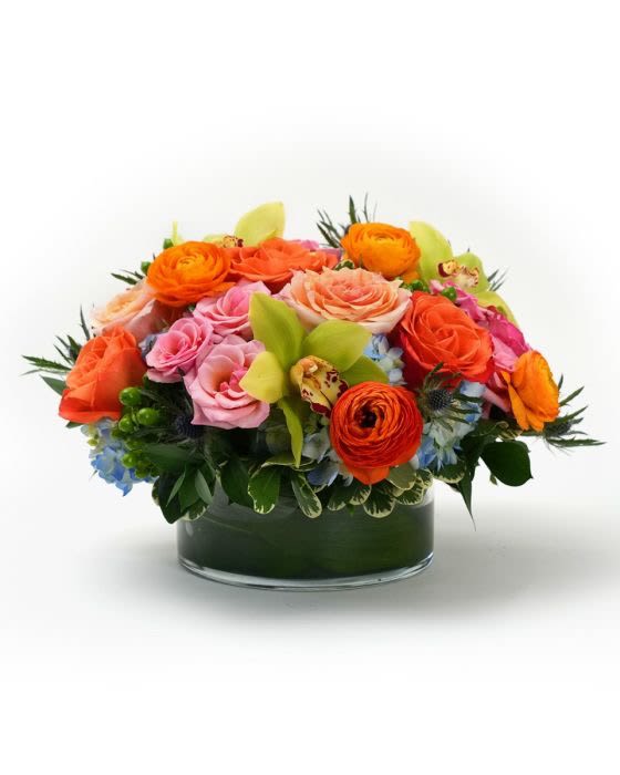 Low arrangement of orange and pink roses with green orchids in a clear glass cylinder vase