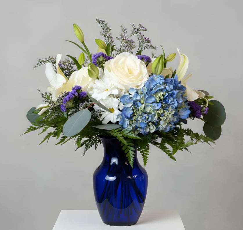 Sapphire Serenity - Cool, graceful, and beautifully refined. Sapphire Serenity pairs crisp whites, soft blues, and rich violet accents in a striking cobalt vase for a design that feels both peaceful and luxurious. A stunning choice for heartfelt sentiments, elegant celebrations, or timeless home décor.