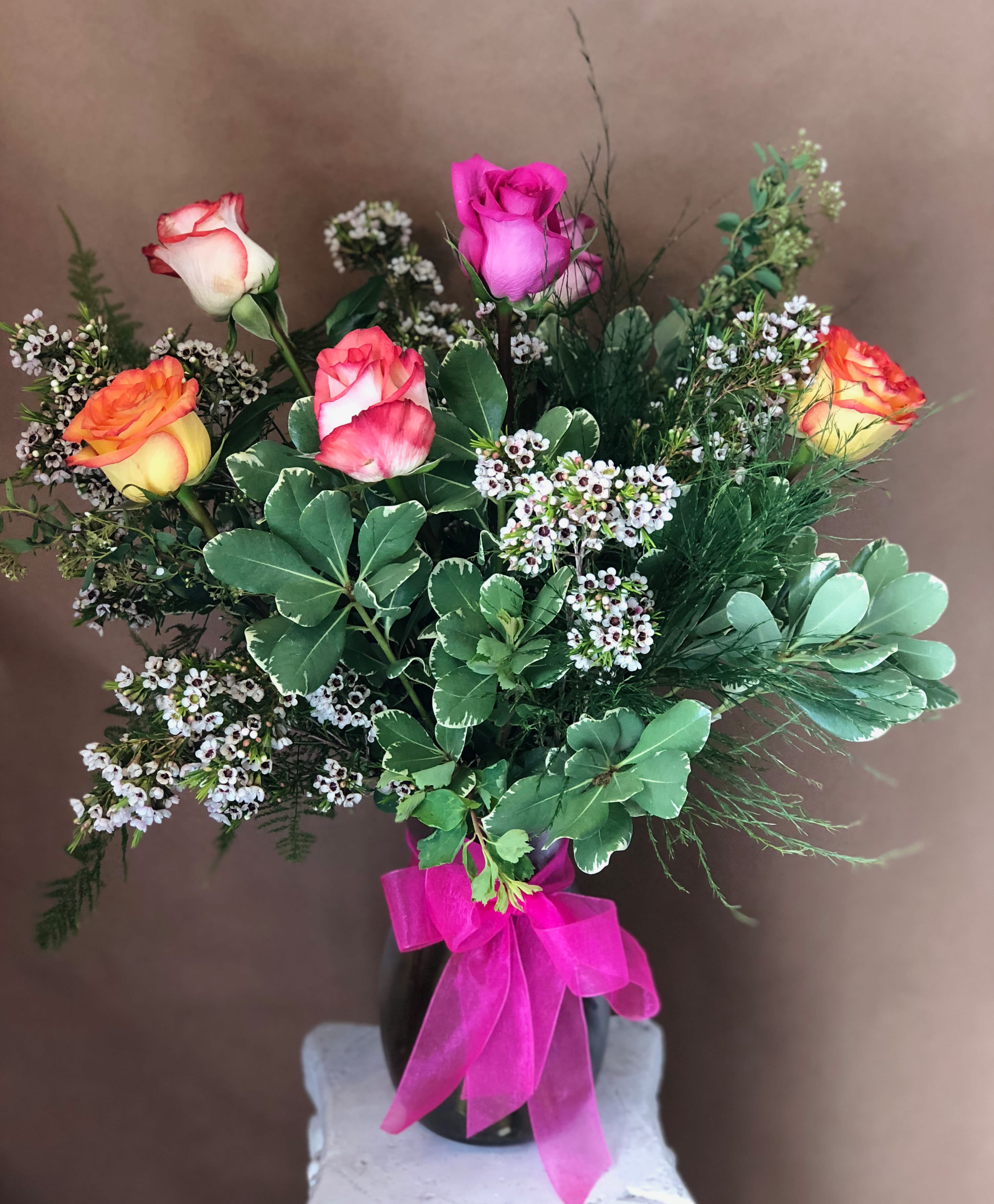 Bouquet of multicolored roses in a black vase with a pink ribbon