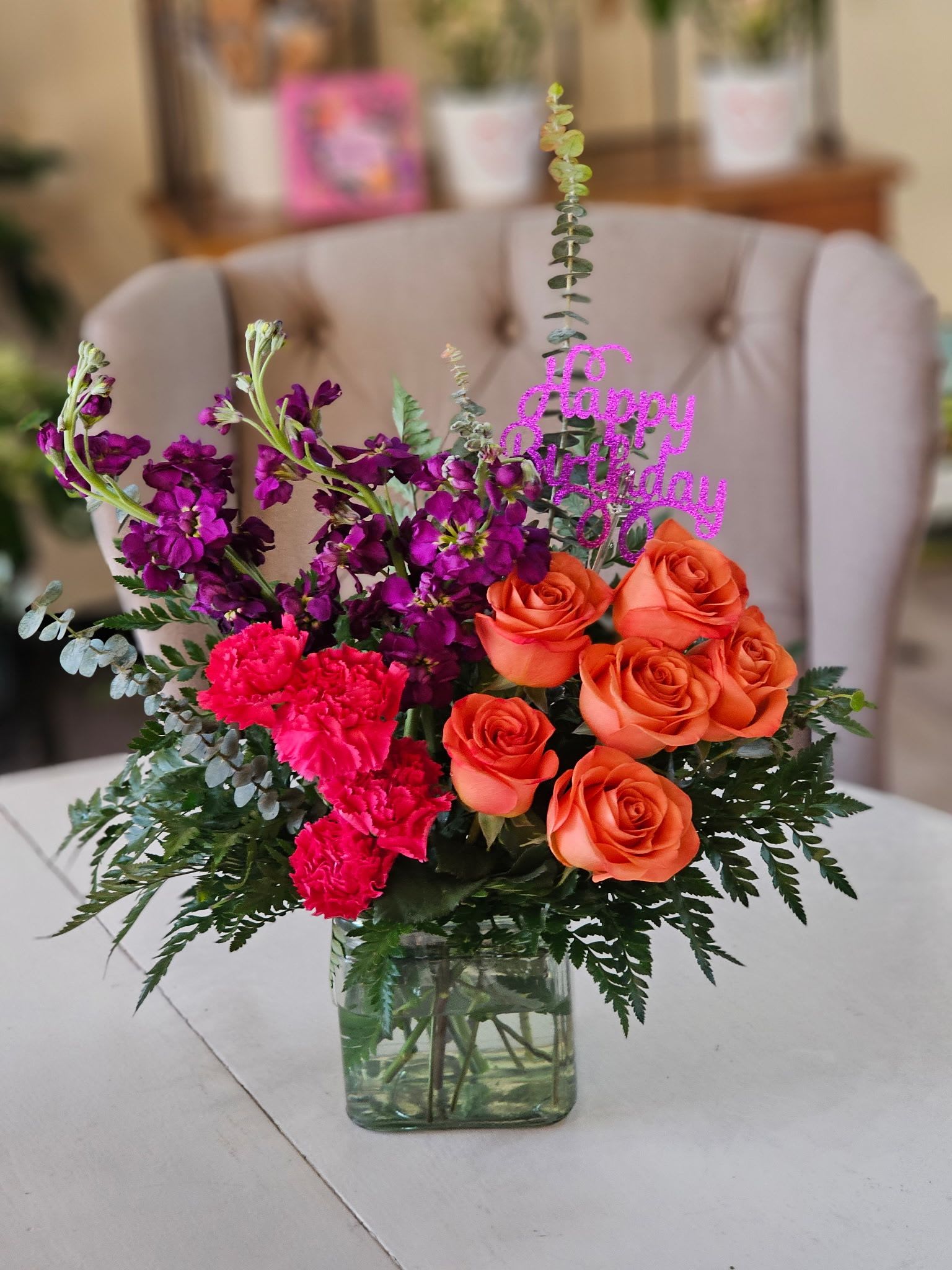 Orange roses and pink flowers in a glass vase with a birthday topper