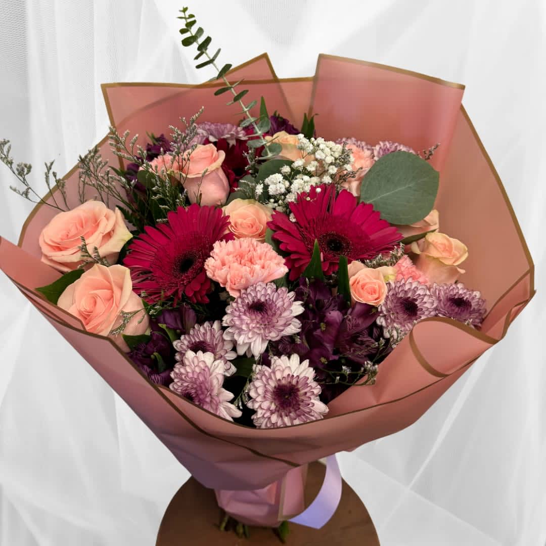Hand-tied bouquet of pink roses, magenta gerbera daisies and lavender mums in pink wrapping