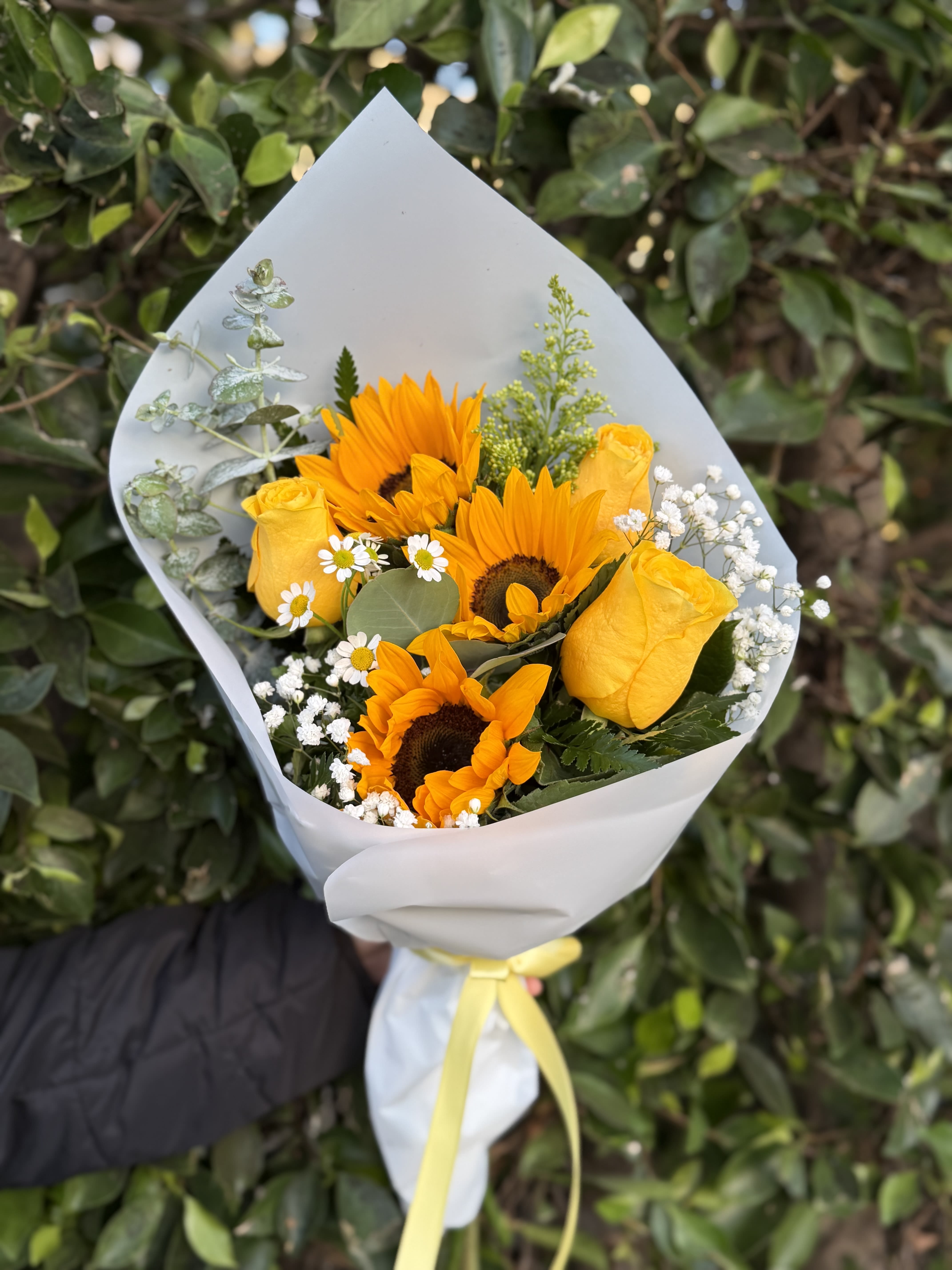 Sunlight  - A radiant wrapped handheld bouquet of sunflowers and yellow roses, accented with delicate filler blooms and fresh eucalyptus. Designed to feel warm, natural, and full of light, Sunlight is a joyful expression of brightness and effortless beauty.
